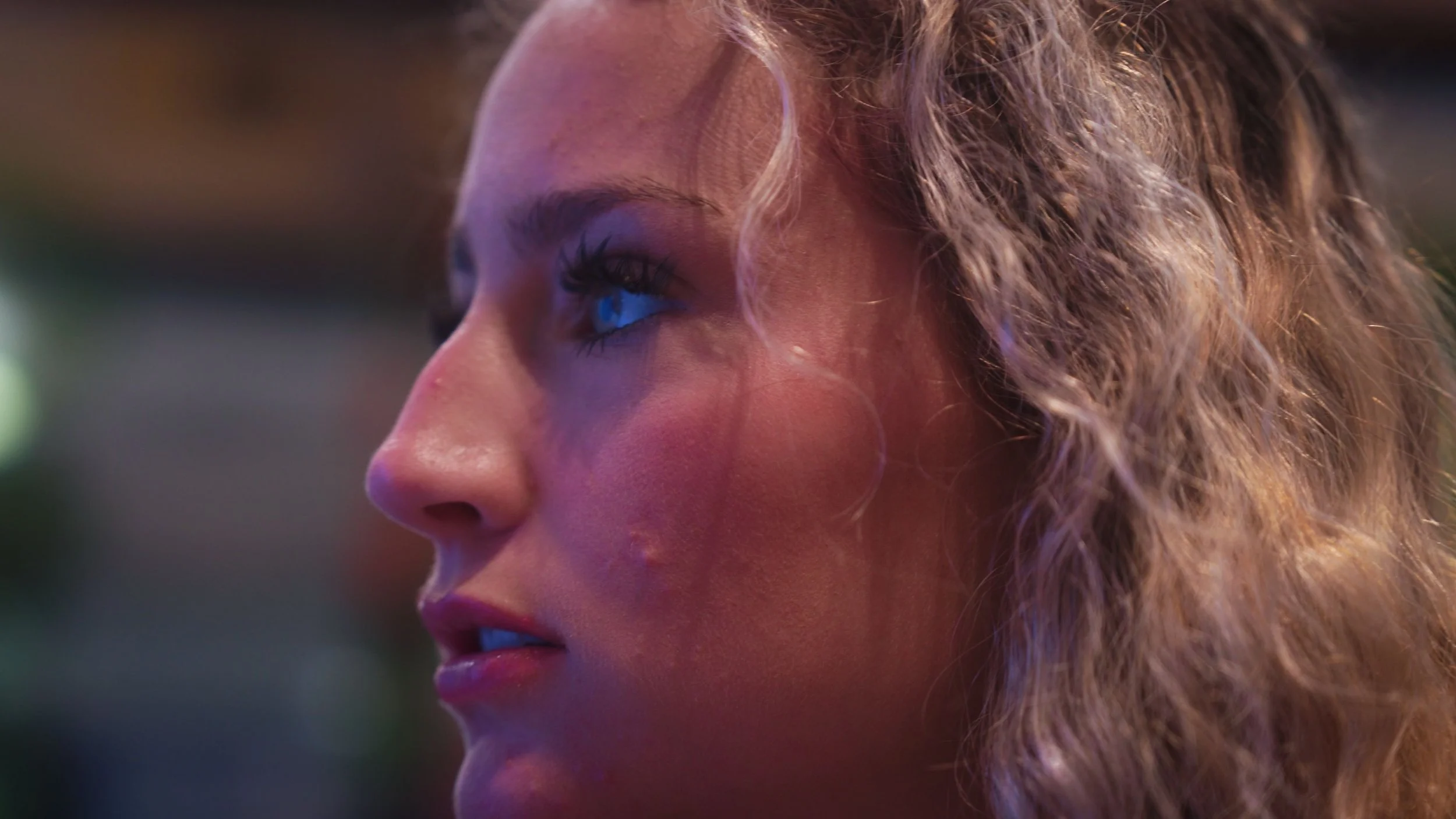 Close-up of a woman with curly hair looking to the side, colorful lighting reflecting on her face.