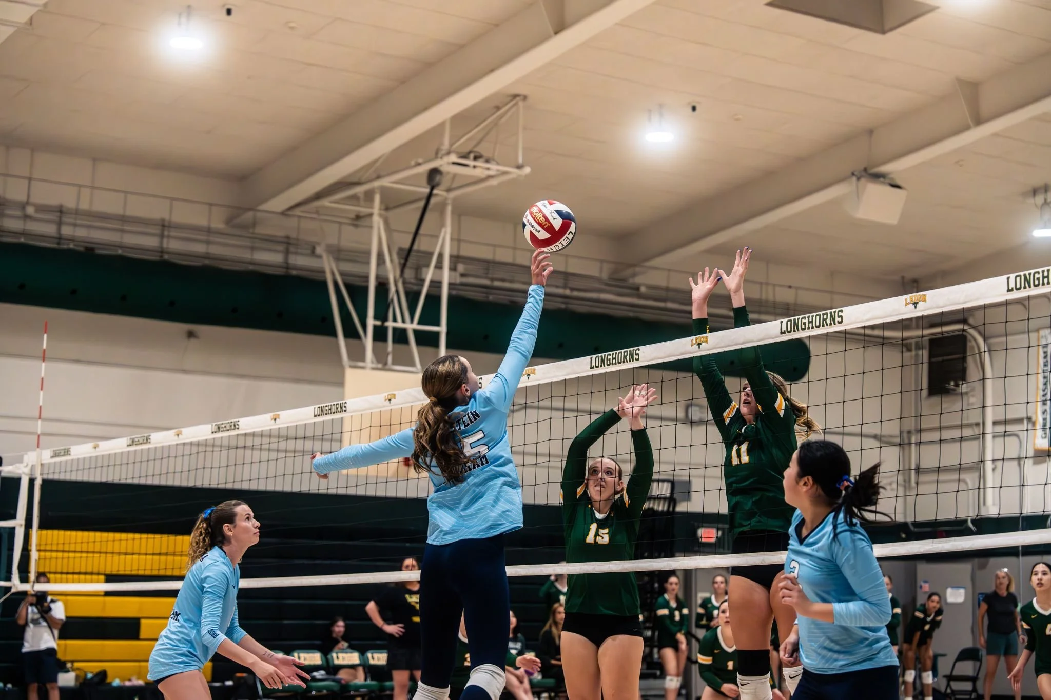 Volleyball players compete at the net during a match in an indoor gymnasium at Longhorns.