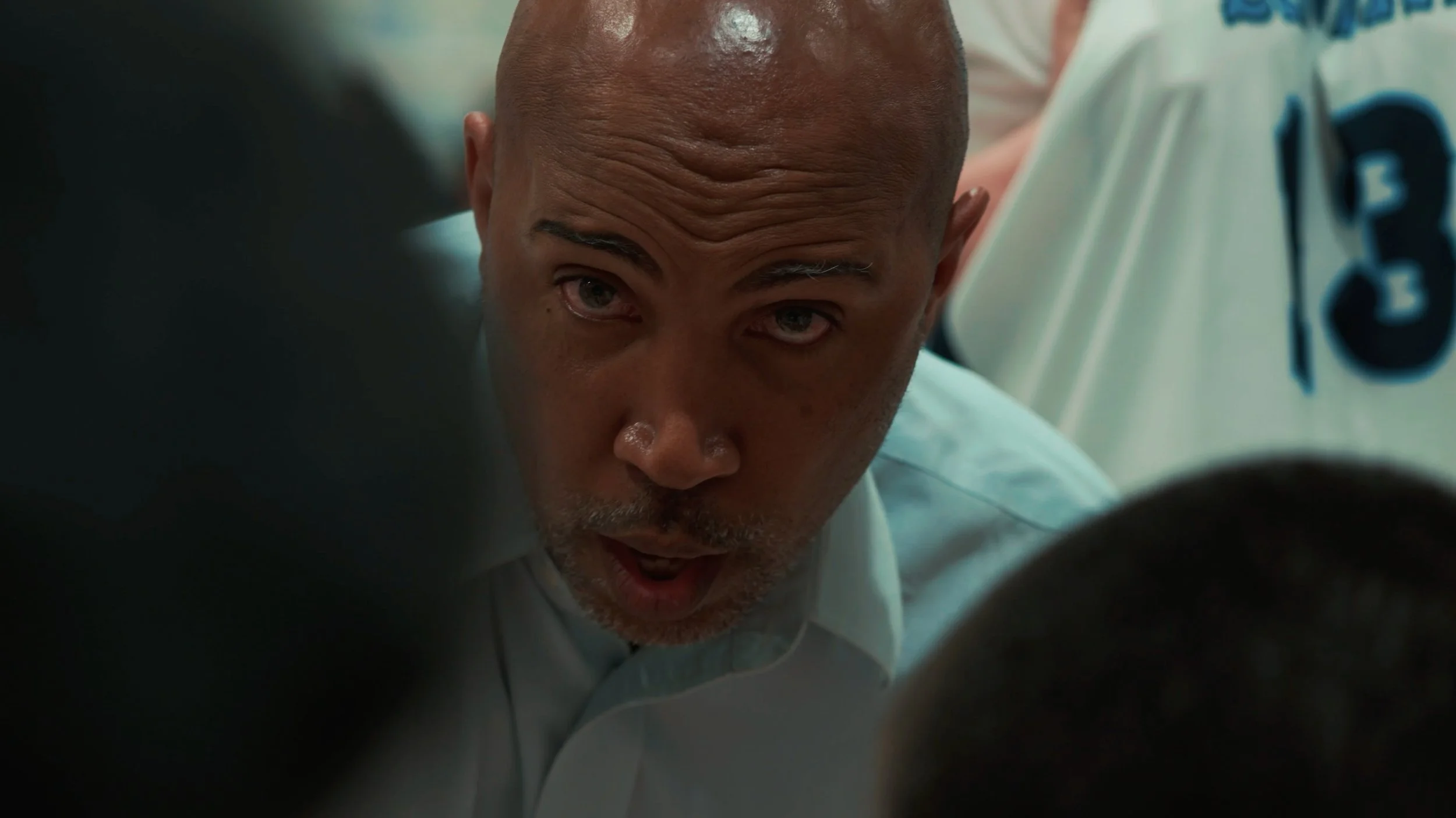 A man with a shaved head and gray beard leaning forward with a focused or surprised expression.