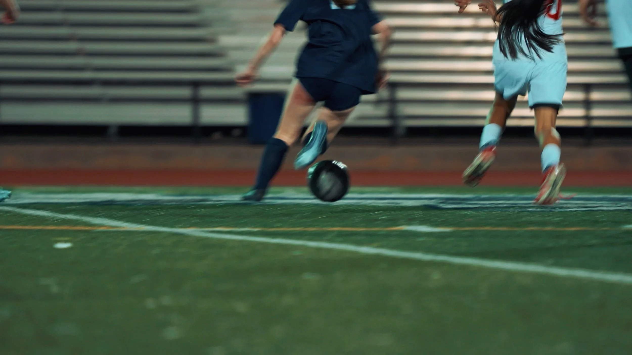 Two children playing soccer on an indoor field, running after the ball with blurred background.