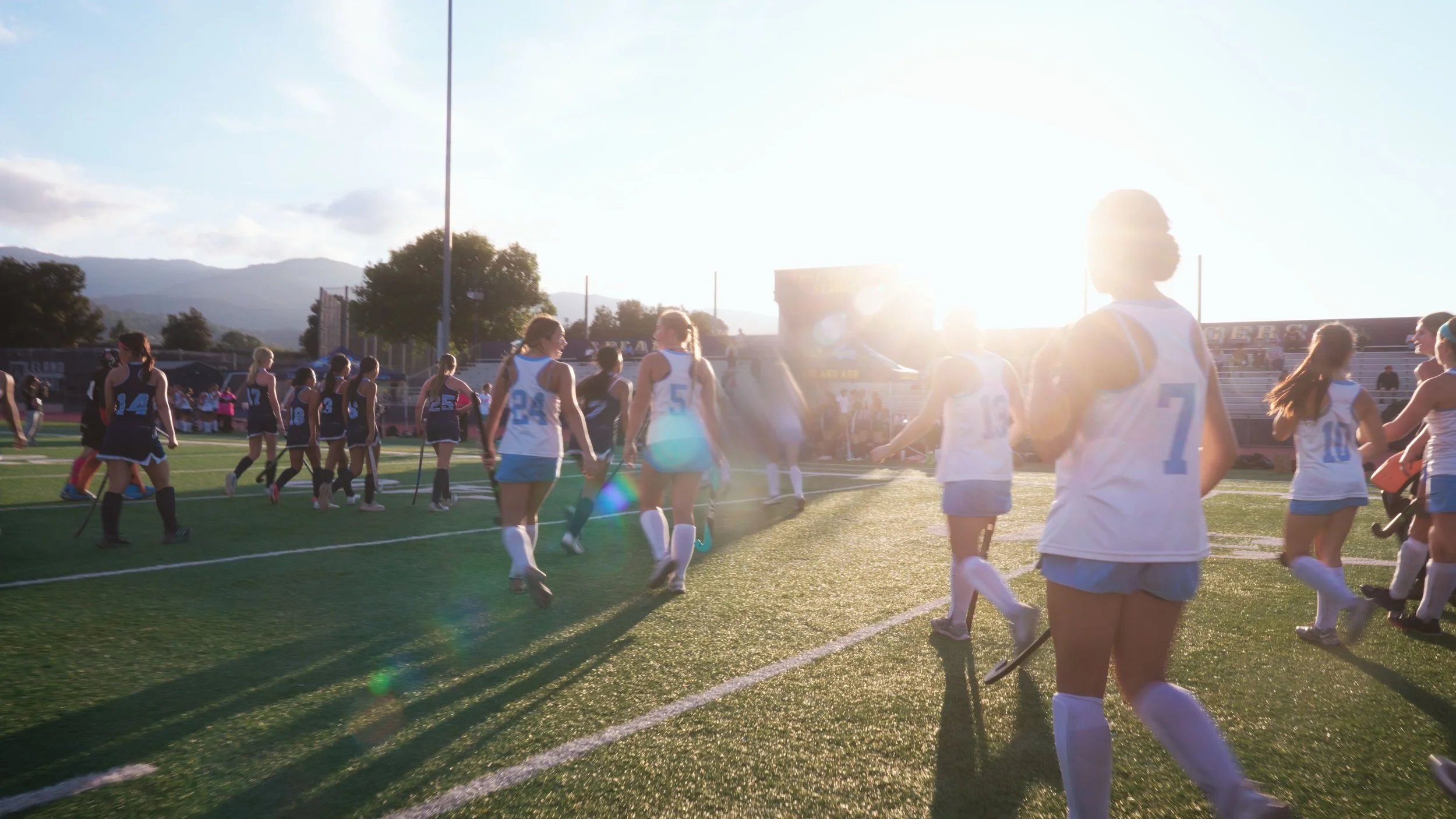 Women’s soccer team walking onto field in sunlight at sunset.
