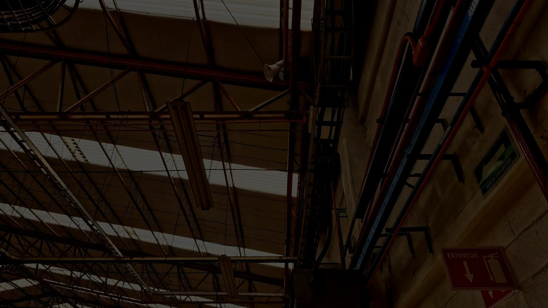 Estructura de escaleras y pasarelas metálicas en un interior industrial con señalización de evacuación y extintor.