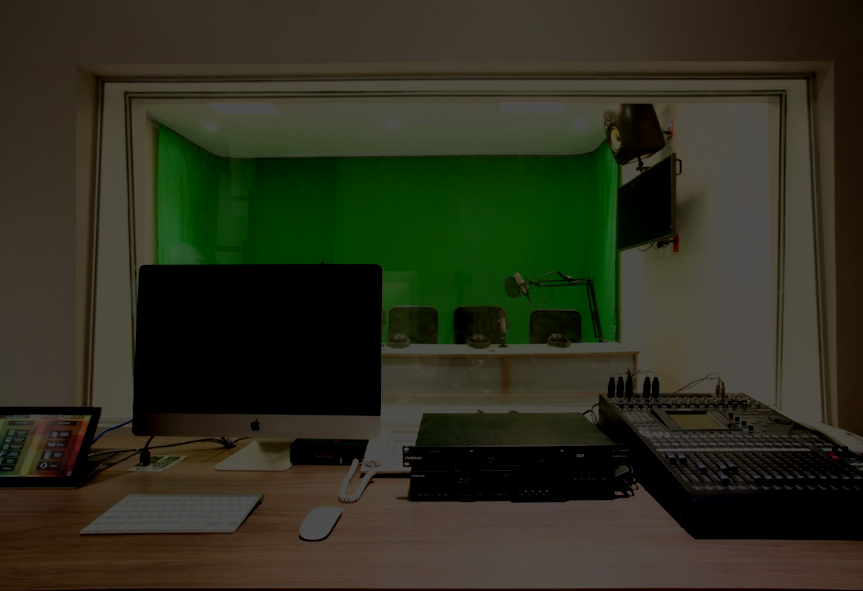 Estudio de grabación con pantalla, teclado, micrófono, consola de audio y ventanas con cortinas verdes.
