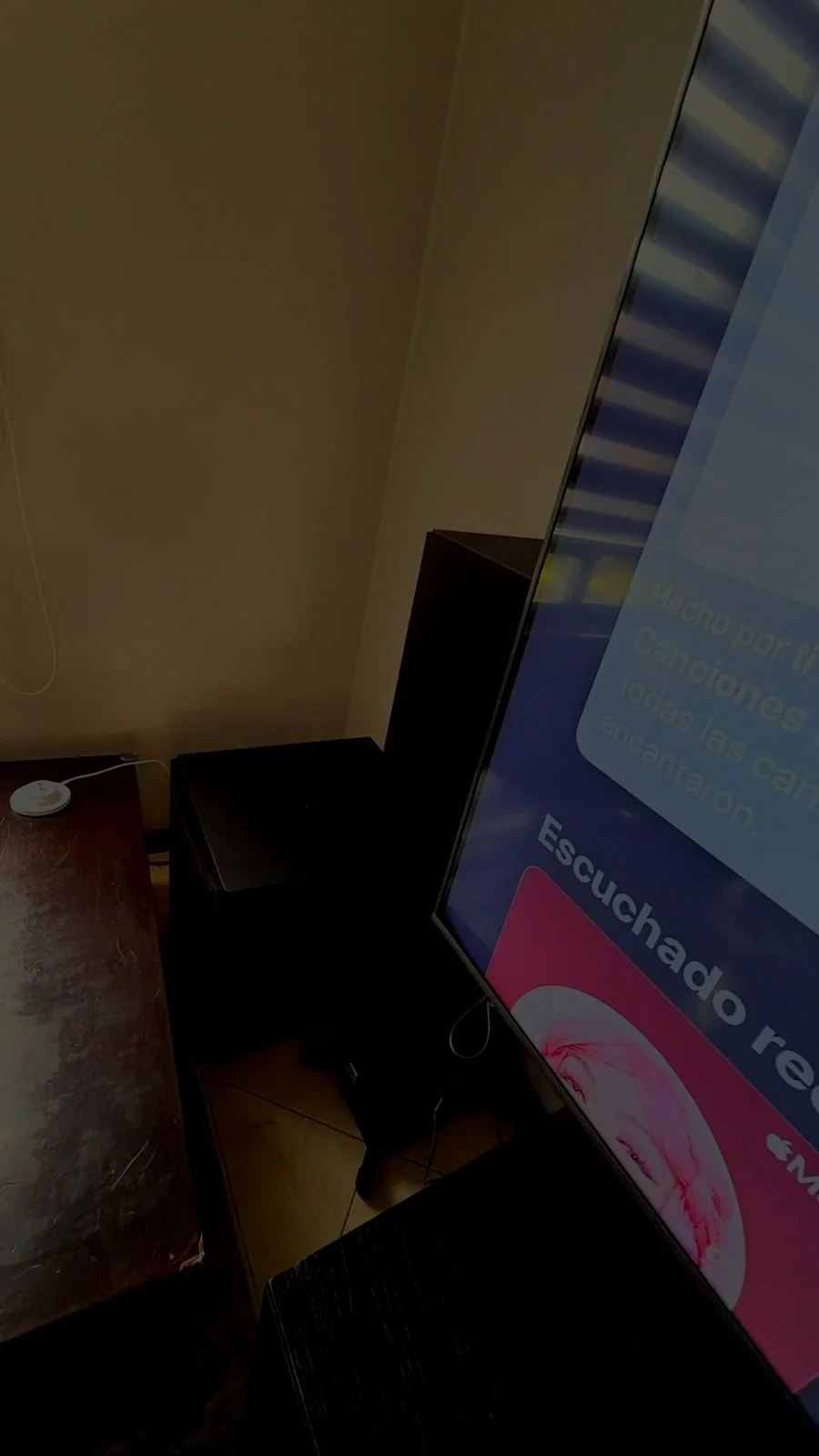 Vista de una sala con una televisión grande que muestra una pantalla azul y rosa, y una pequeña caja negra en el suelo, junto a un mueble de madera oscura y una pared beige.