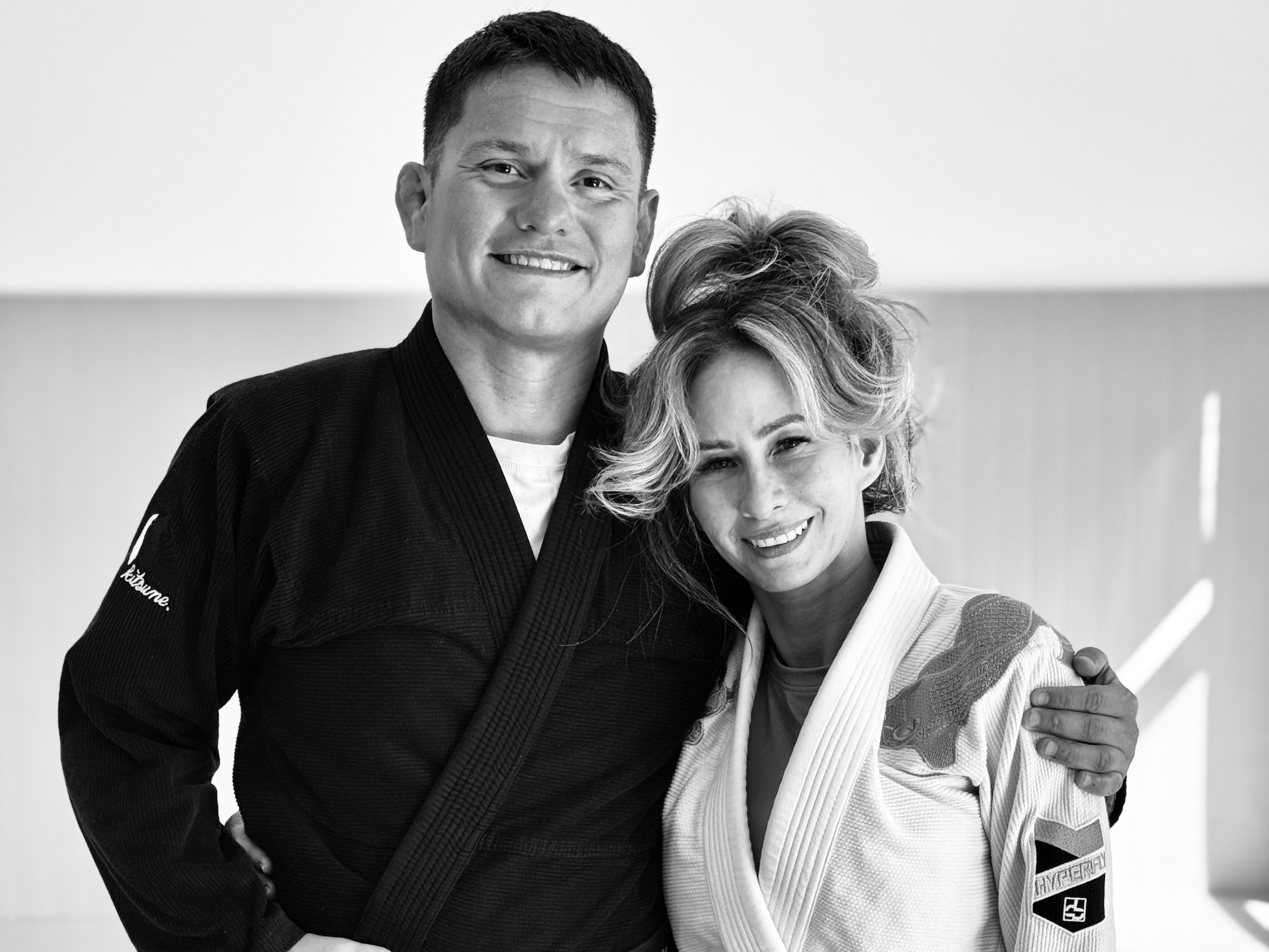 Black and white photo of a man and a woman in jiu jitsu uniforms smiling and embracing each other.