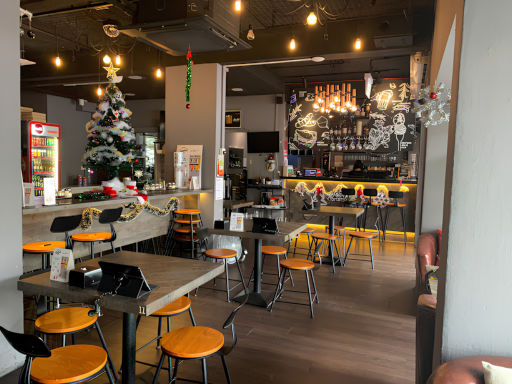 Interior of a cafe decorated for Christmas with a Christmas tree, holiday garlands, and festive lights, featuring tables and chairs, a counter with coffee and snacks, and a chalkboard wall with drawings.