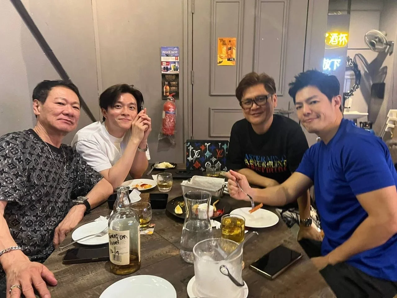 Four men sitting at a table in a restaurant or bar, enjoying food and drinks.