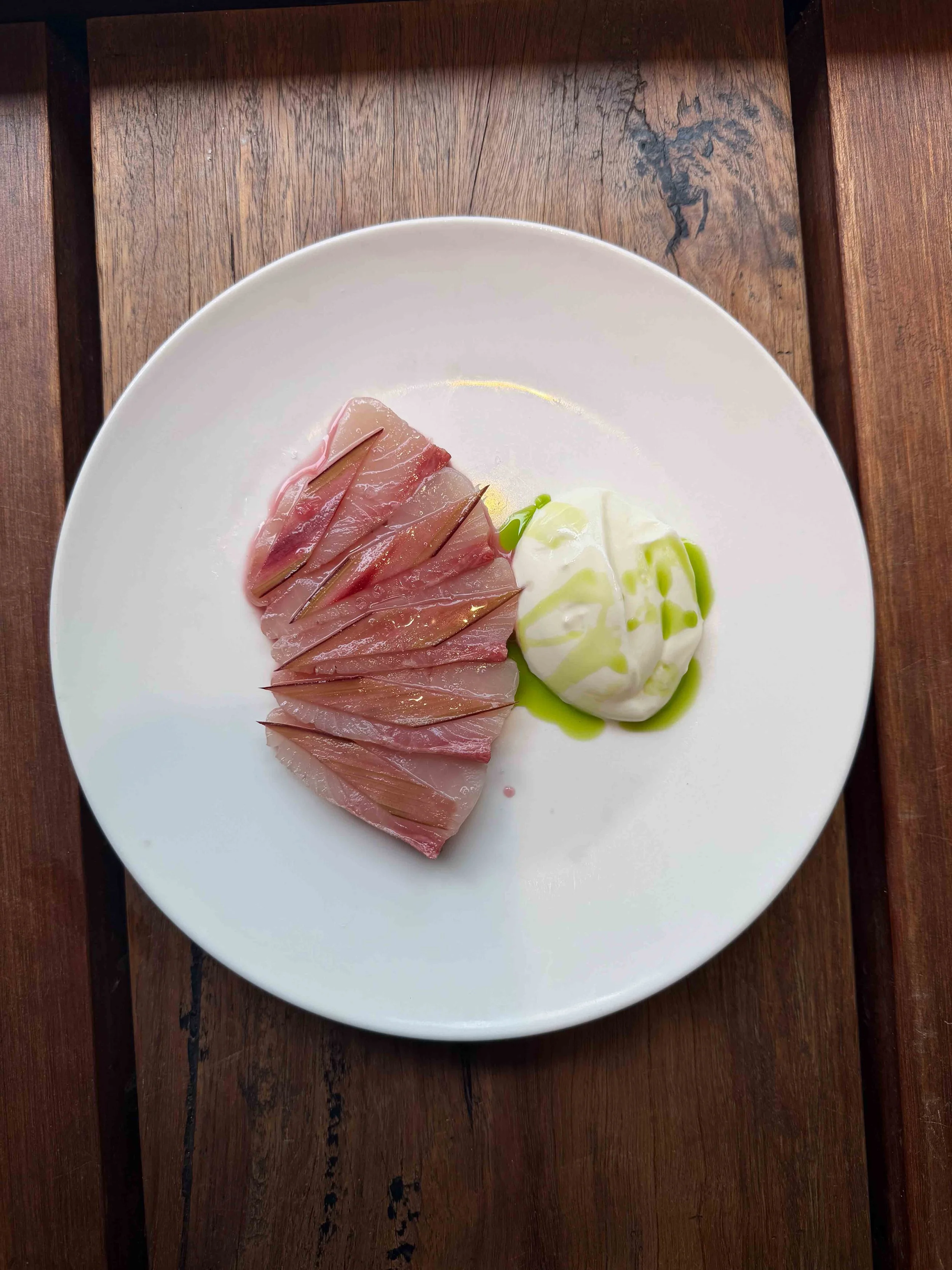 Sliced cured ham with a ball of mozzarella cheese and green sauce on a white plate.