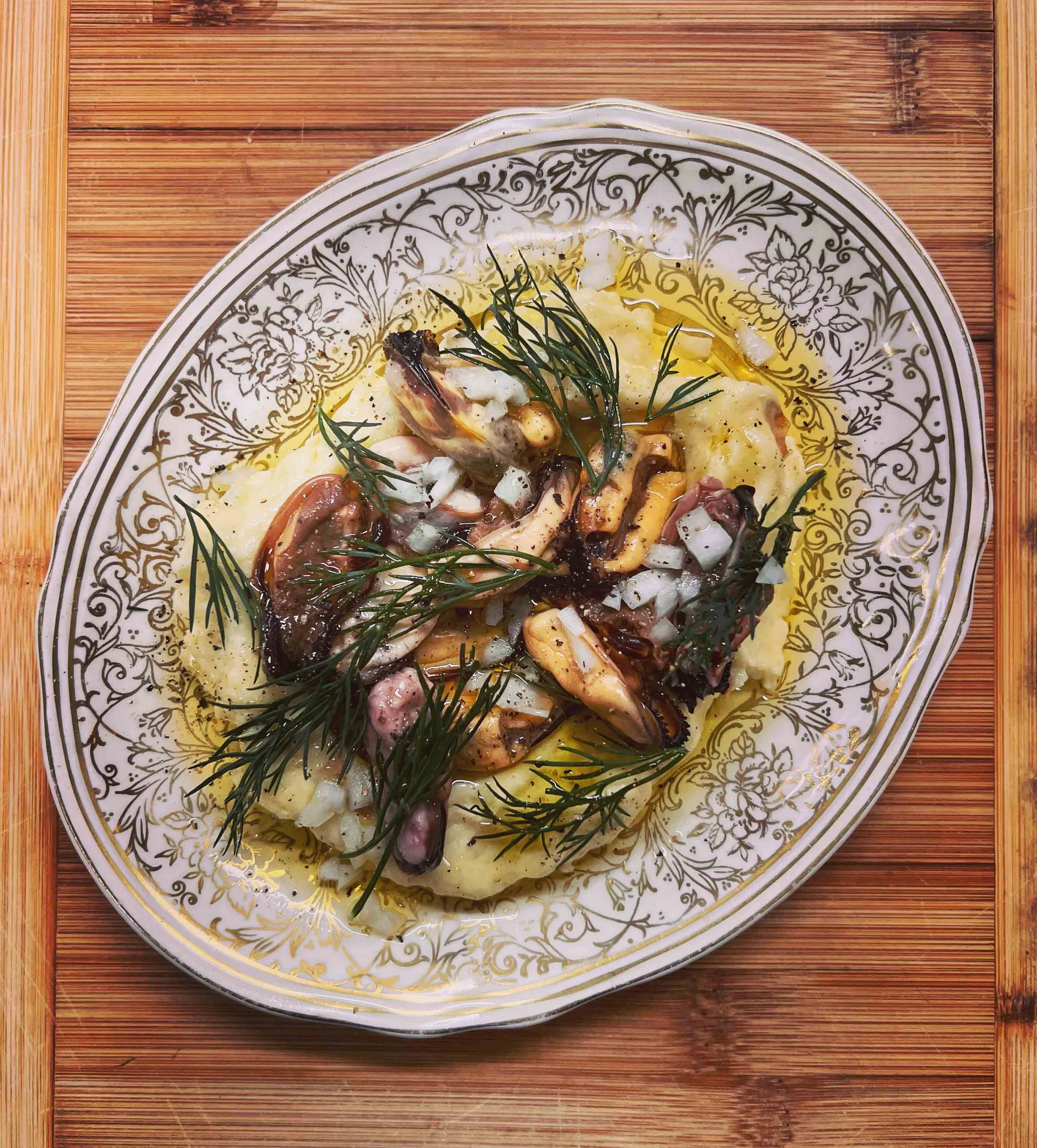 A decorative white and gold plate with food, topped with herbs, placed on a wooden surface.