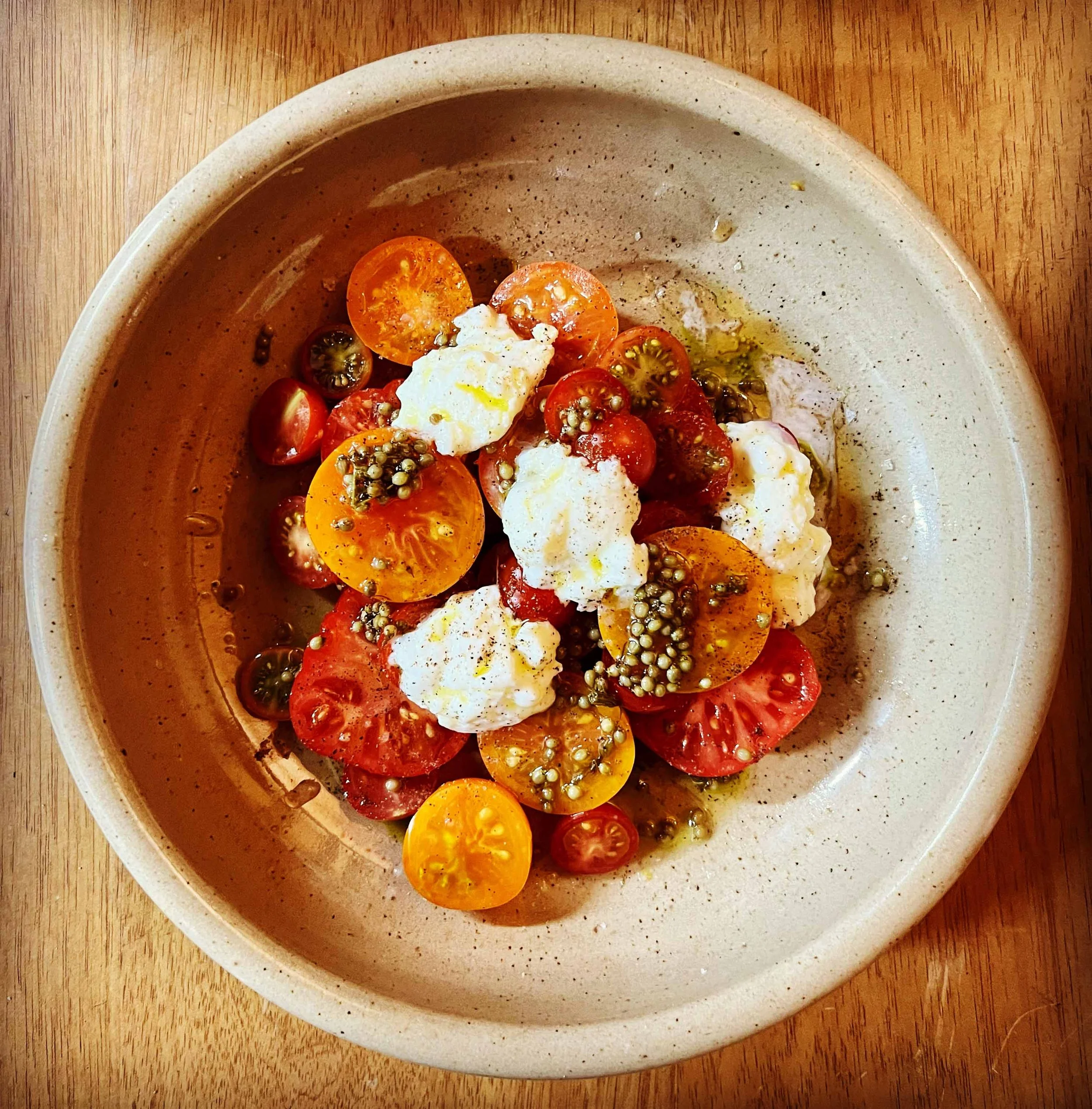 A bowl of cherry tomatoes with some mayonnaise or cream and black pepper on top, placed on a wooden surface.