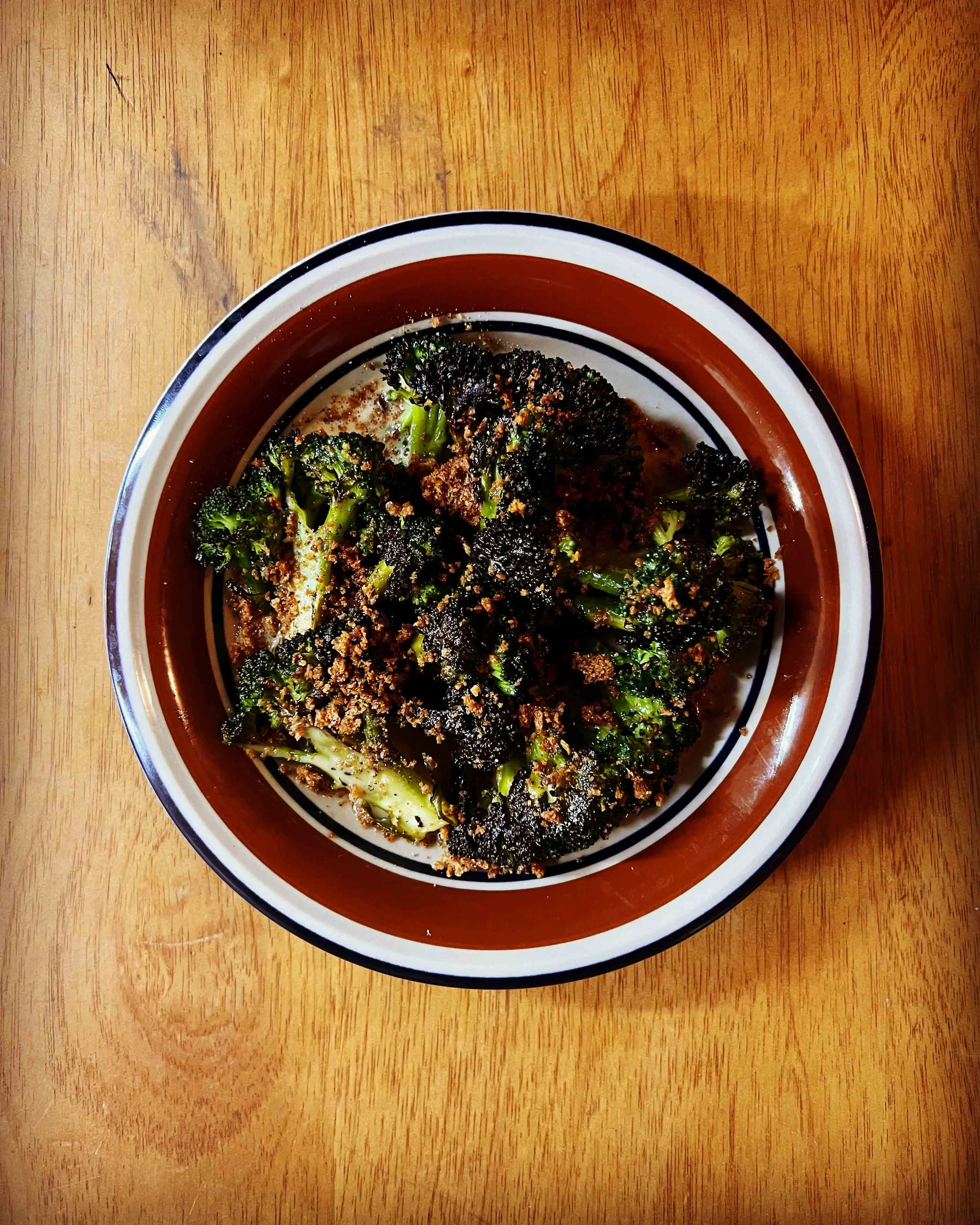 A bowl of roasted broccoli with a sprinkle of spices on a wooden table.