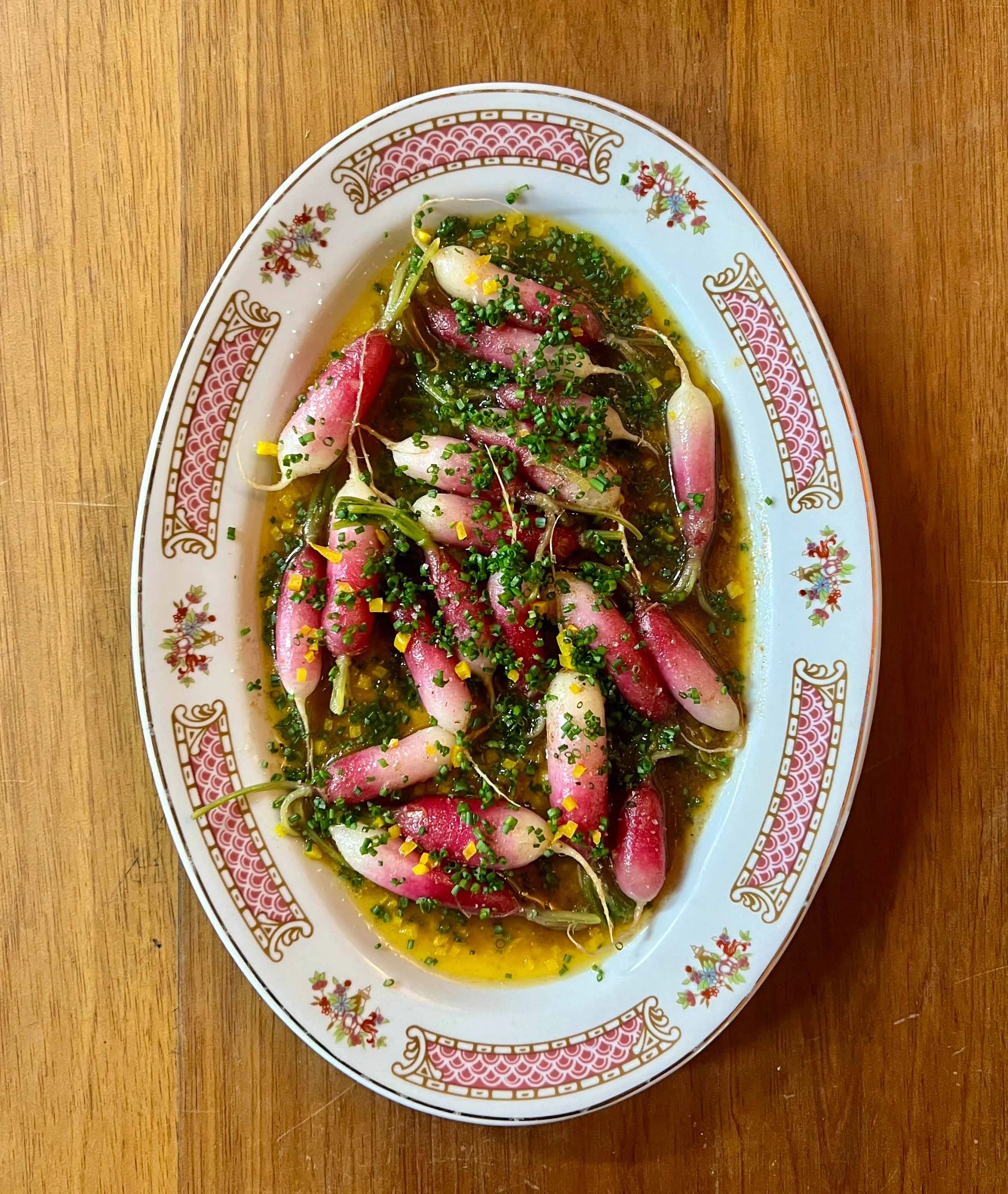 Plate of cooked radishes garnished with chopped herbs and yellow zest on a decorative ceramic plate.