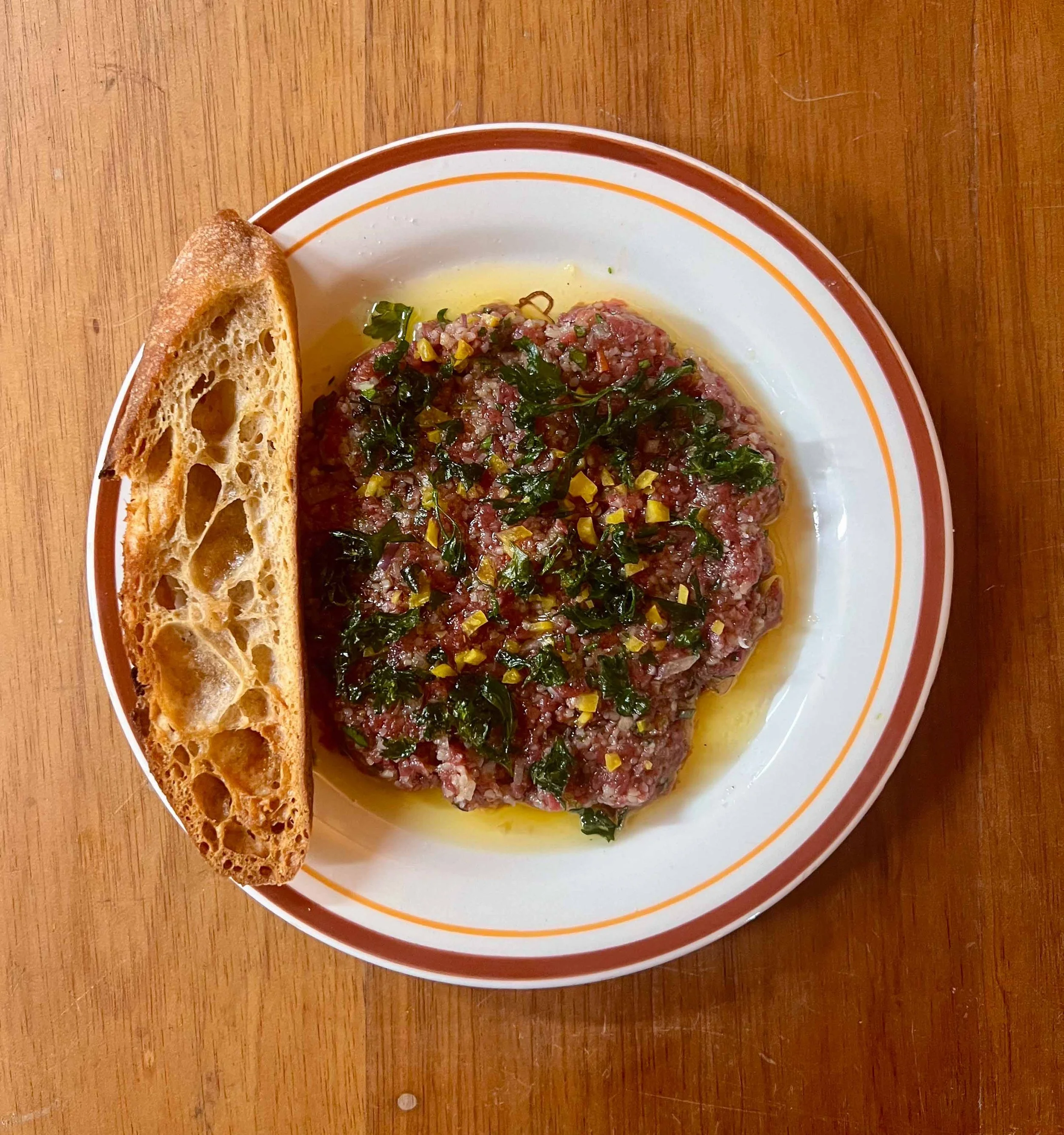 Plate of steak tartare garnished with herbs and served with a side of bread on a wooden table.
