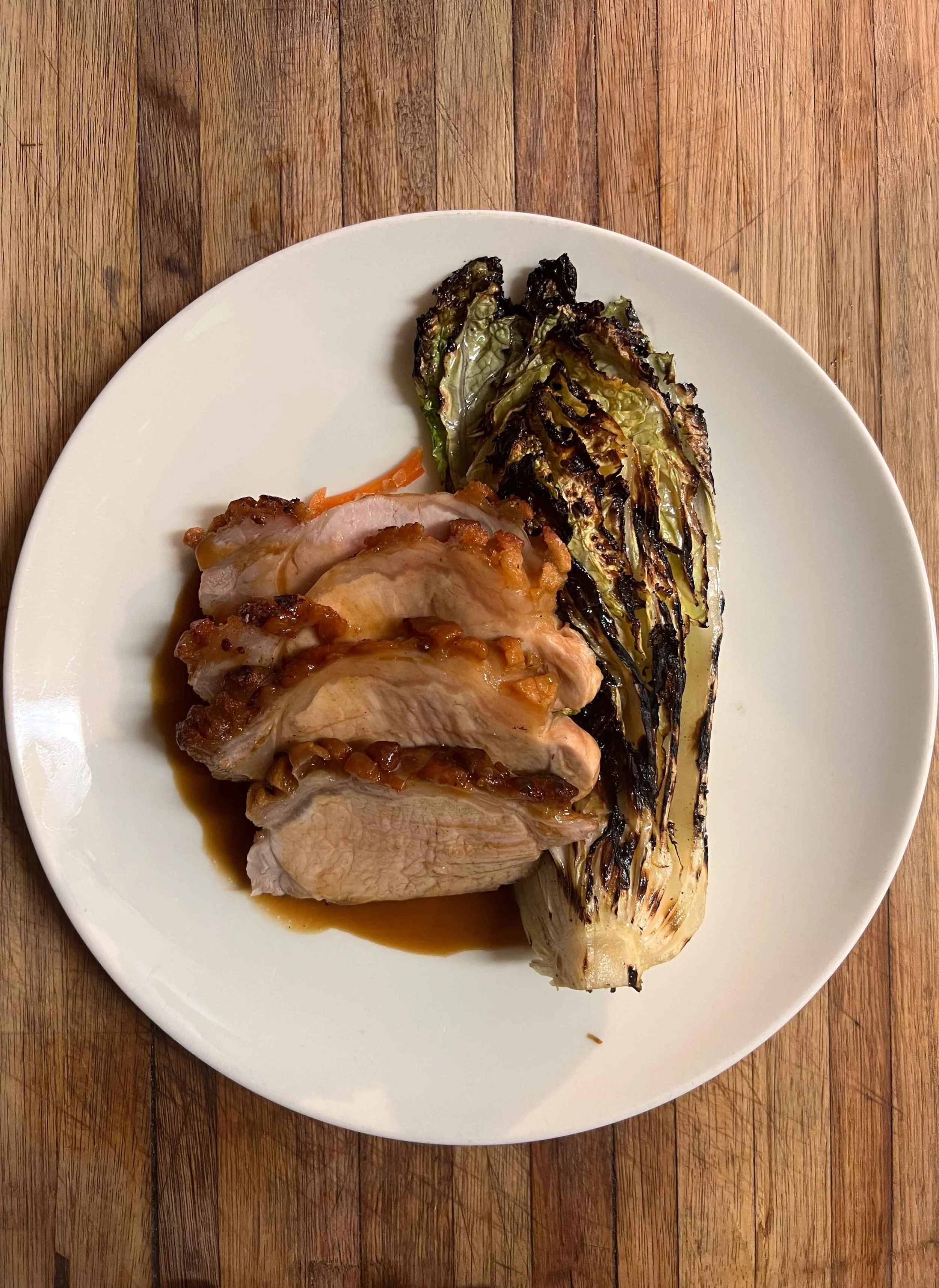 A white plate with cooked chicken breast, roasted romaine lettuce, and a dipping sauce on a wooden table.