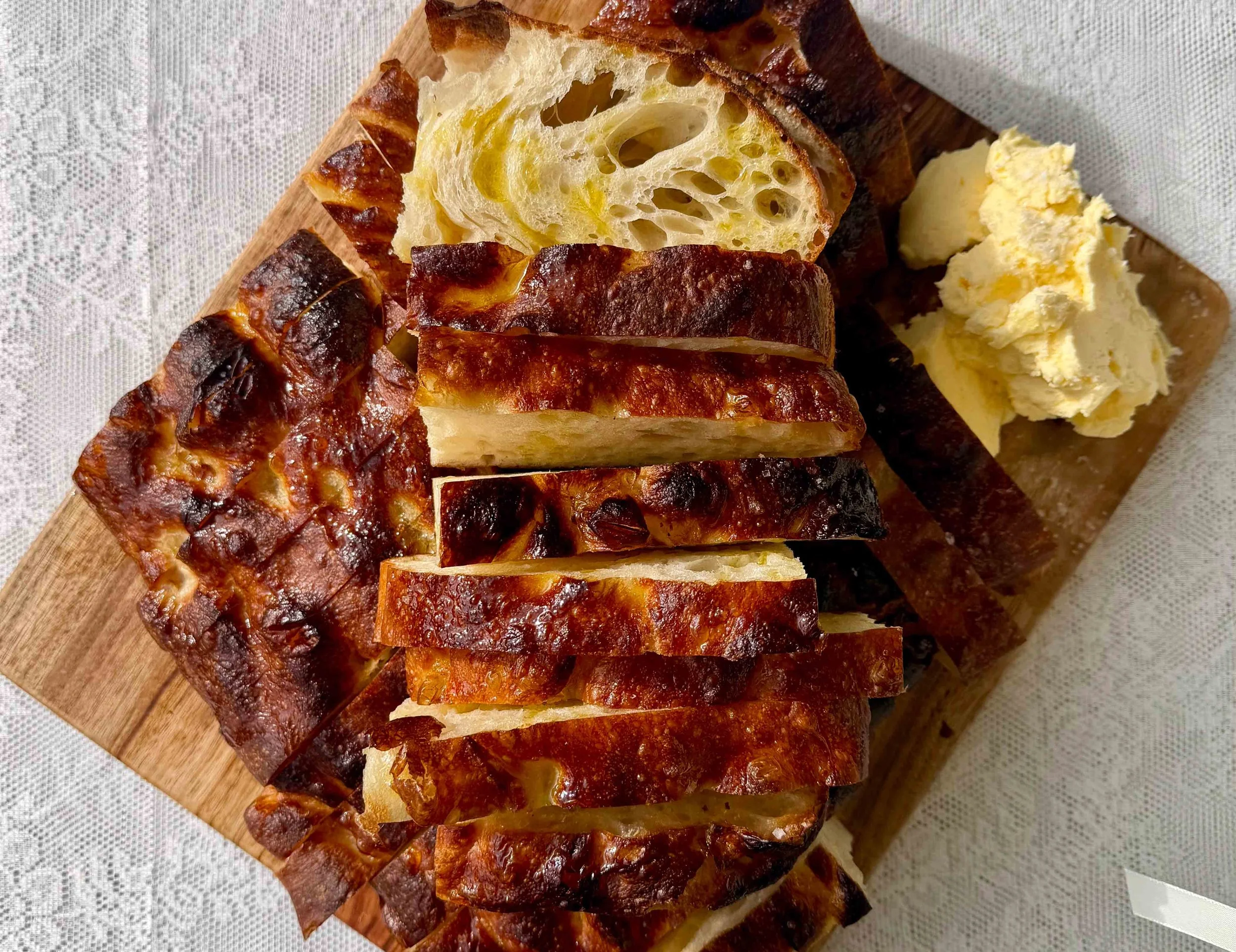 A loaf of bread sliced on a wooden cutting board with a side of butter or spread.