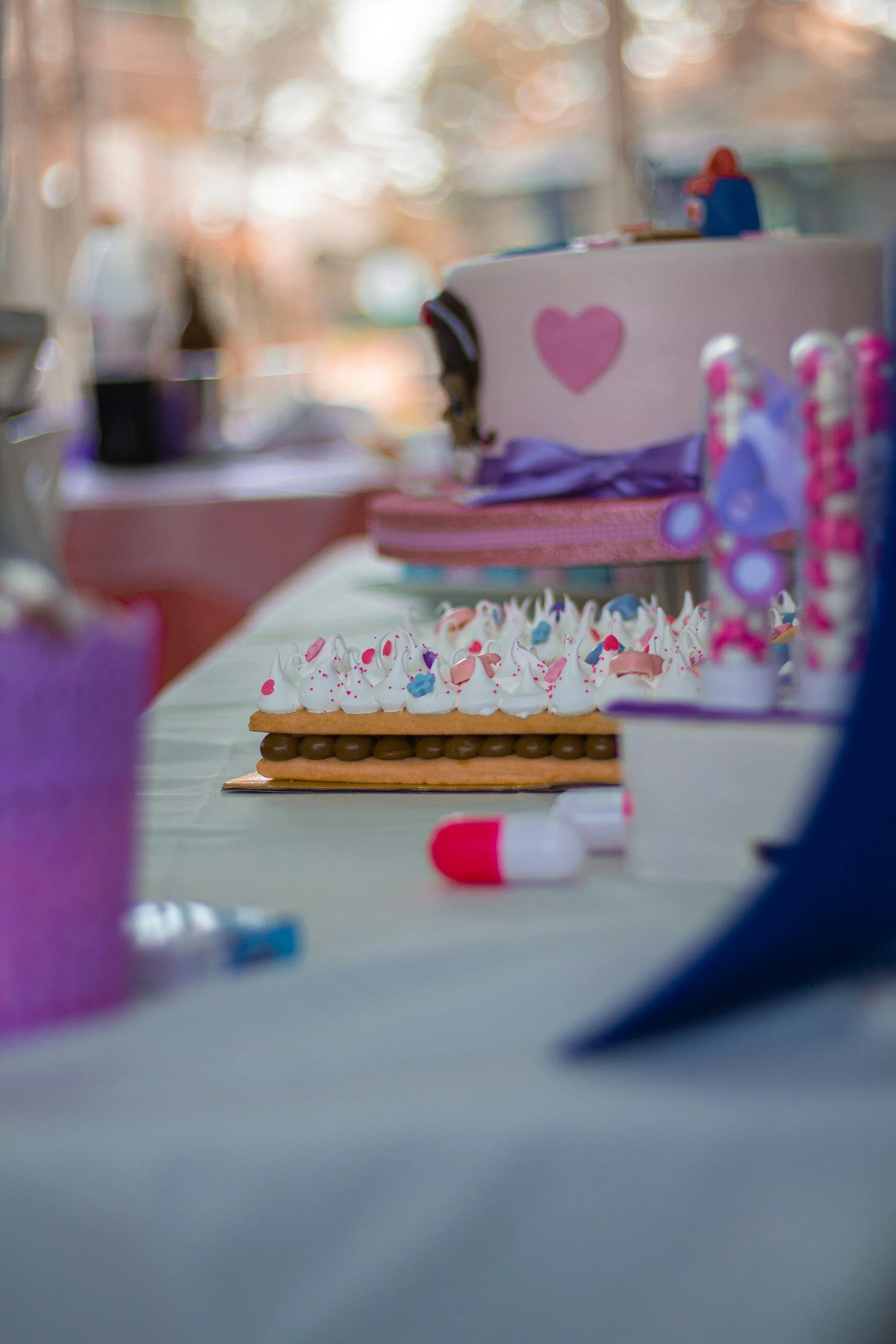 Decorated dessert with whipped cream, colorful sprinkles, and a cookie on a table, with birthday cake in the background.