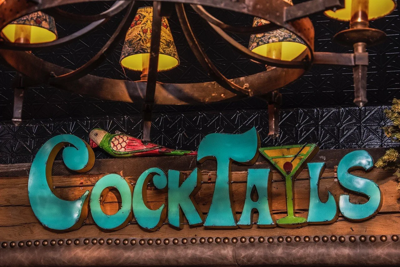 Colorful sign that reads 'Cocktails' with a decorative fish on top and a stylized martini glass replacing the letter 'I'.