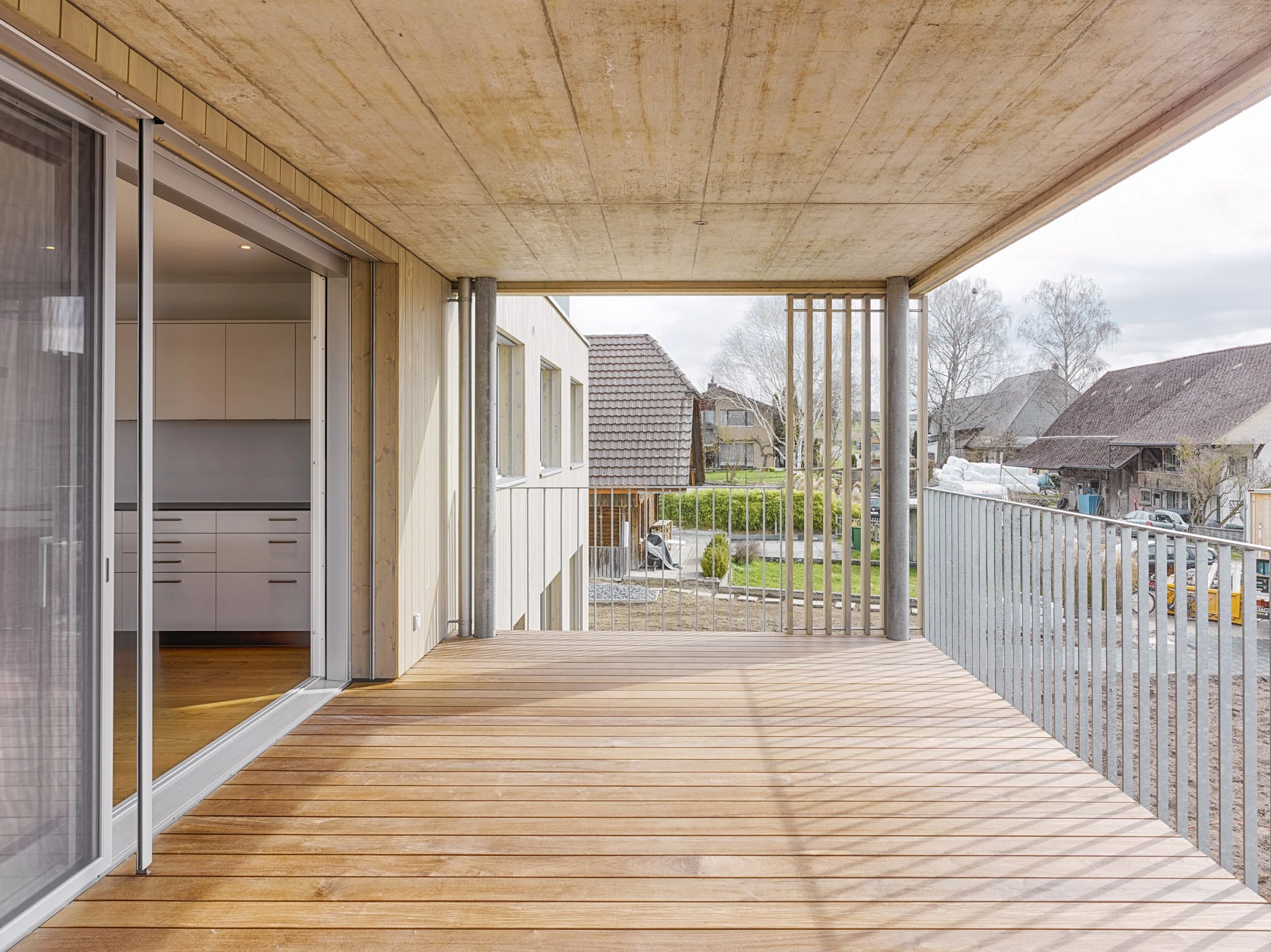 Holzterrasse mit Geländer und Blick auf Nachbarhäuser im Hintergrund.