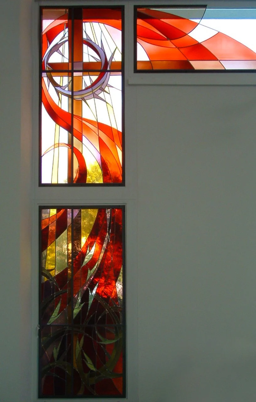 Bunte Glasfenster mit abstrakten roten, orange, gelb und lila Mustern in einer Kirche.