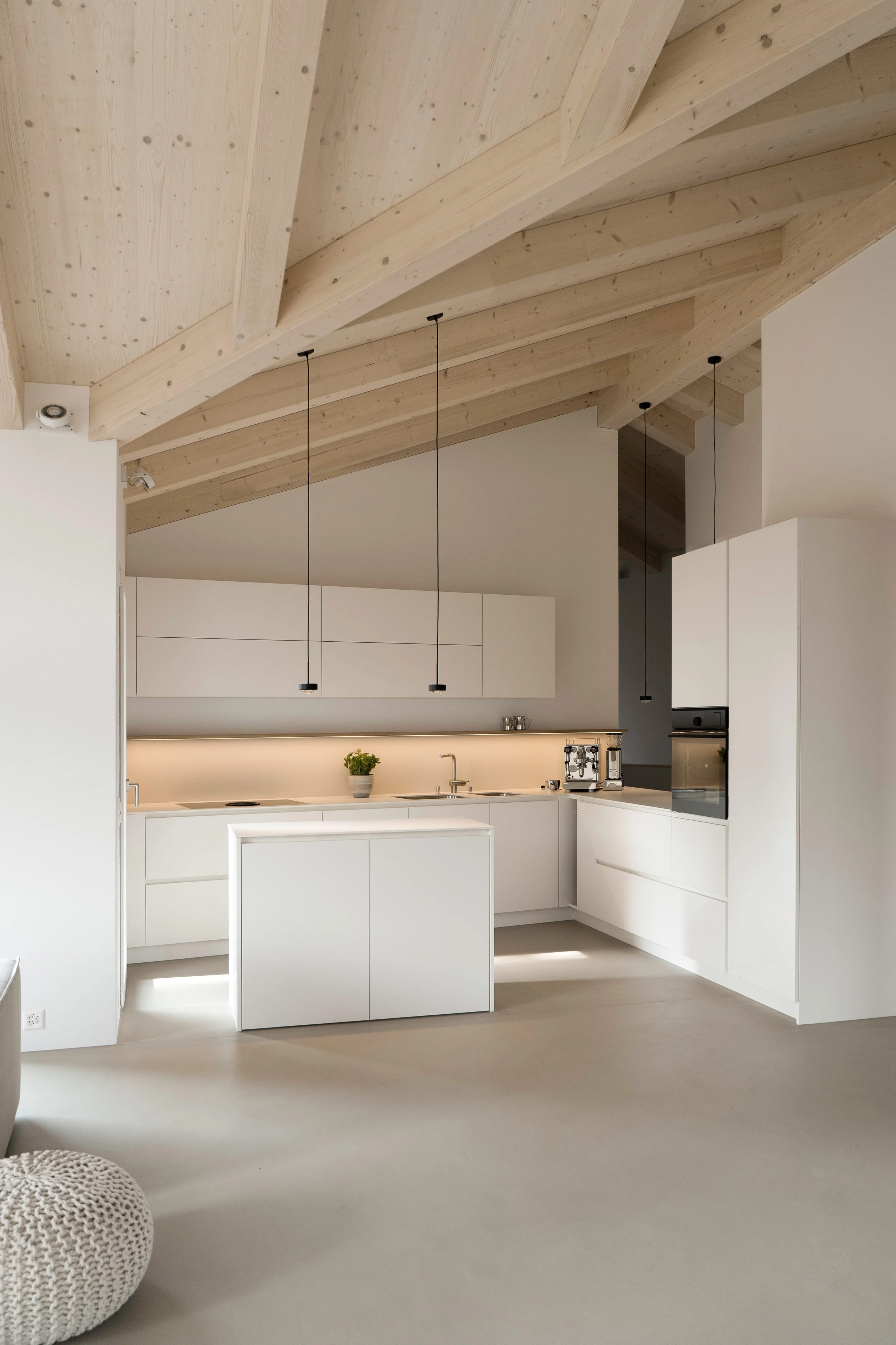Moderne weiße Küche mit Holzdecke und leichten Punkten, minimalistisches Design, Hängebeleuchtung, kleiner Pflanze auf der Arbeitsfläche, unscharfer Hocker im Vordergrund.