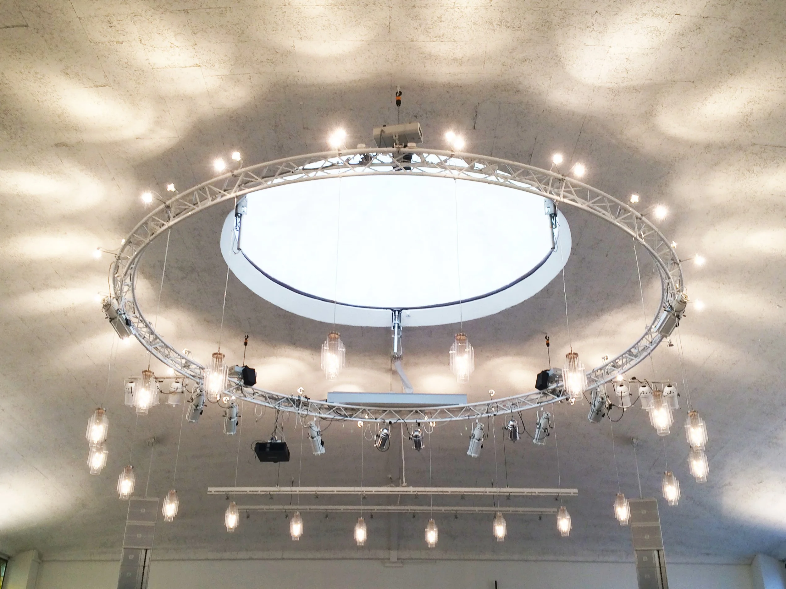 Blick nach oben auf eine große runde Musik- oder Bühnendekoration mit Beleuchtung an einer Halledecke.