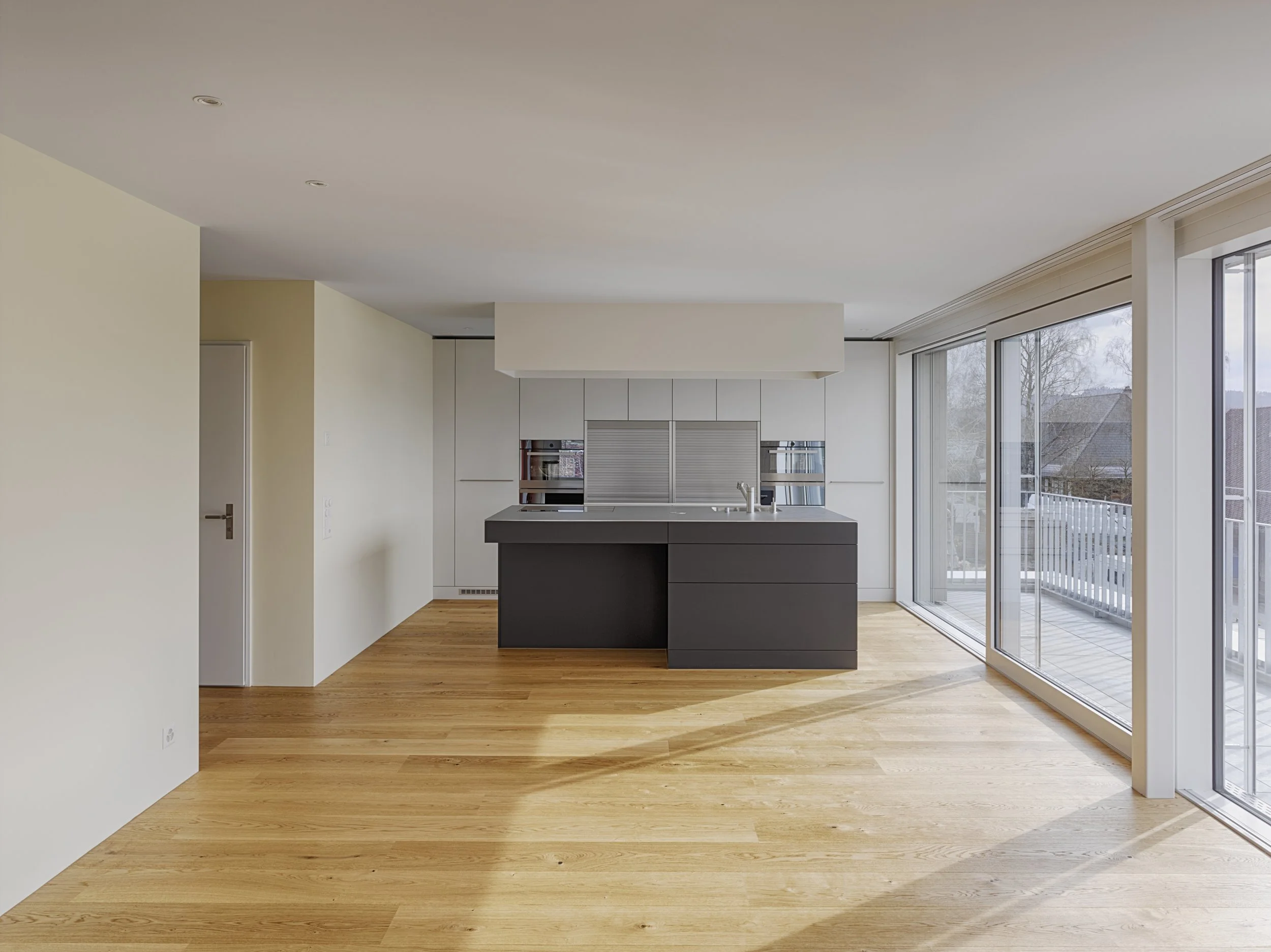 Offene moderne Küche mit Insel, große Fenster, Holzboden, weiße Wände