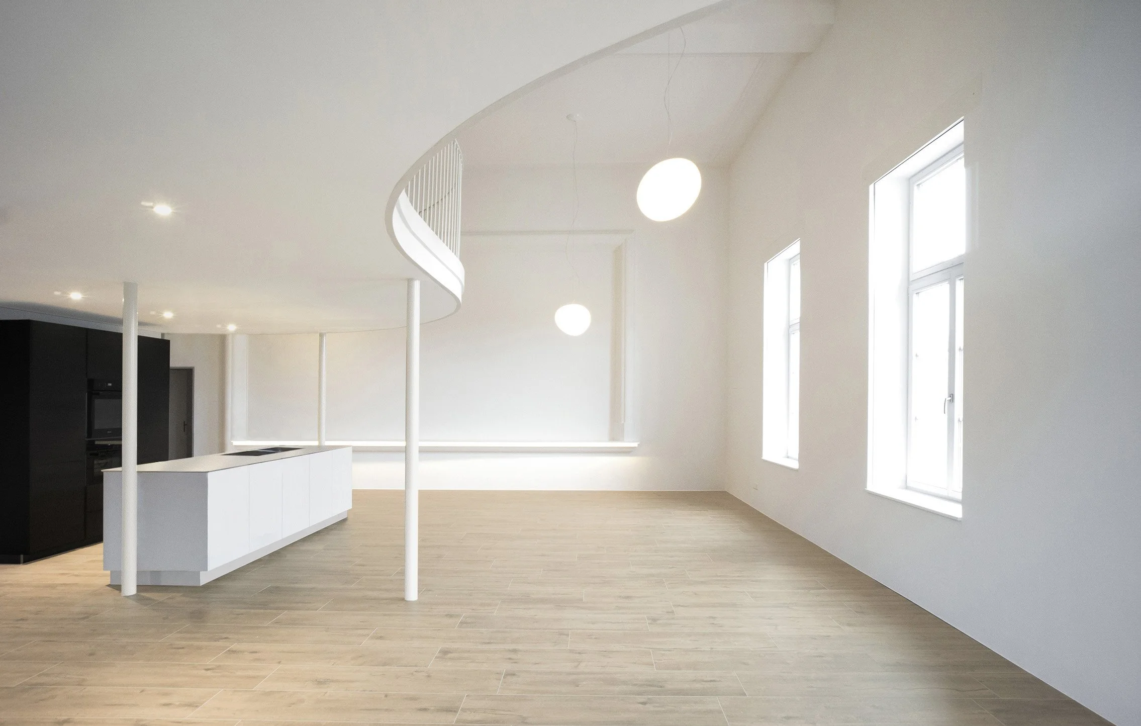 Ein heller, moderner Raum mit großen Fenstern, weißen Wänden, Holzfußboden und minimalistischer Gestaltung.