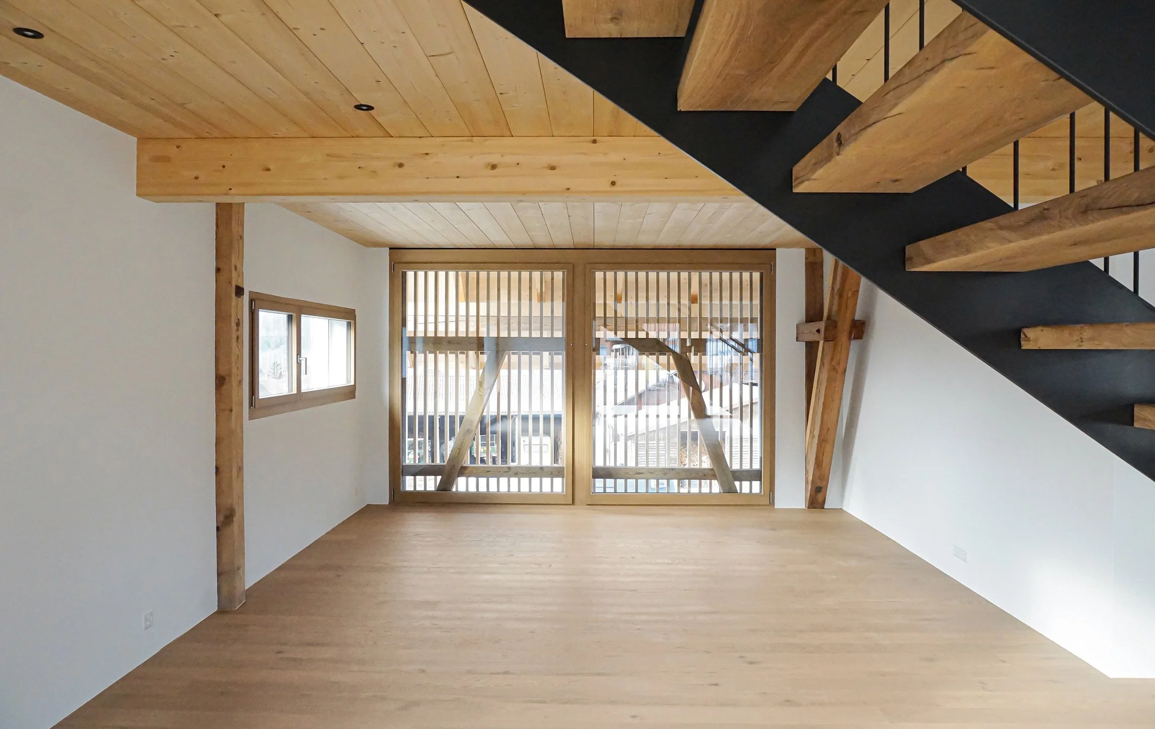 Innenansicht eines helle Holzhauses mit Holztreppe und großer Glasfront, viel natürlicher Licht durch Fenster