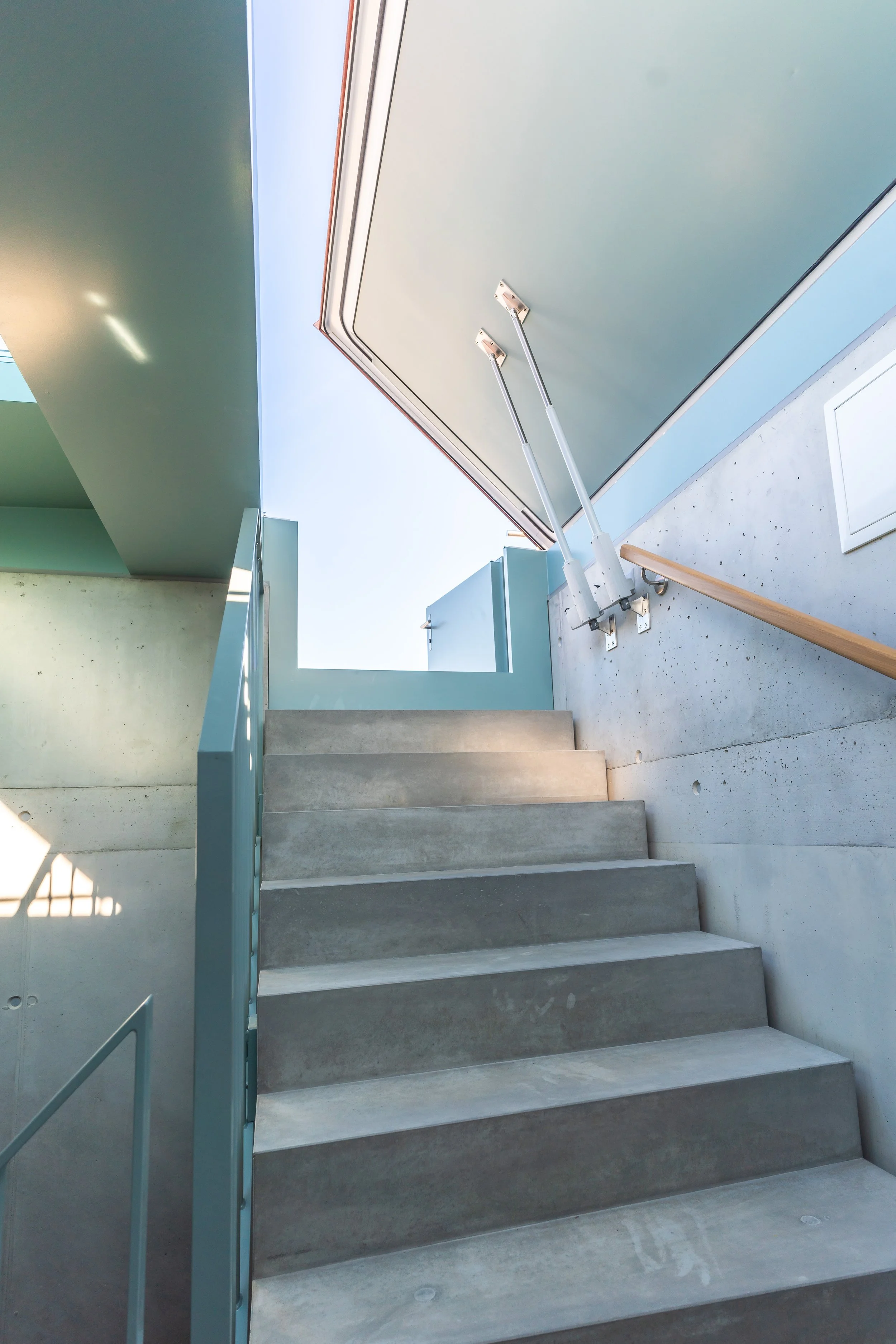 Stufen einer modernen Treppe aus Beton mit blauer metallischer Handlauf, im Hintergrund ein blauer Himmel und Gebäudeteile