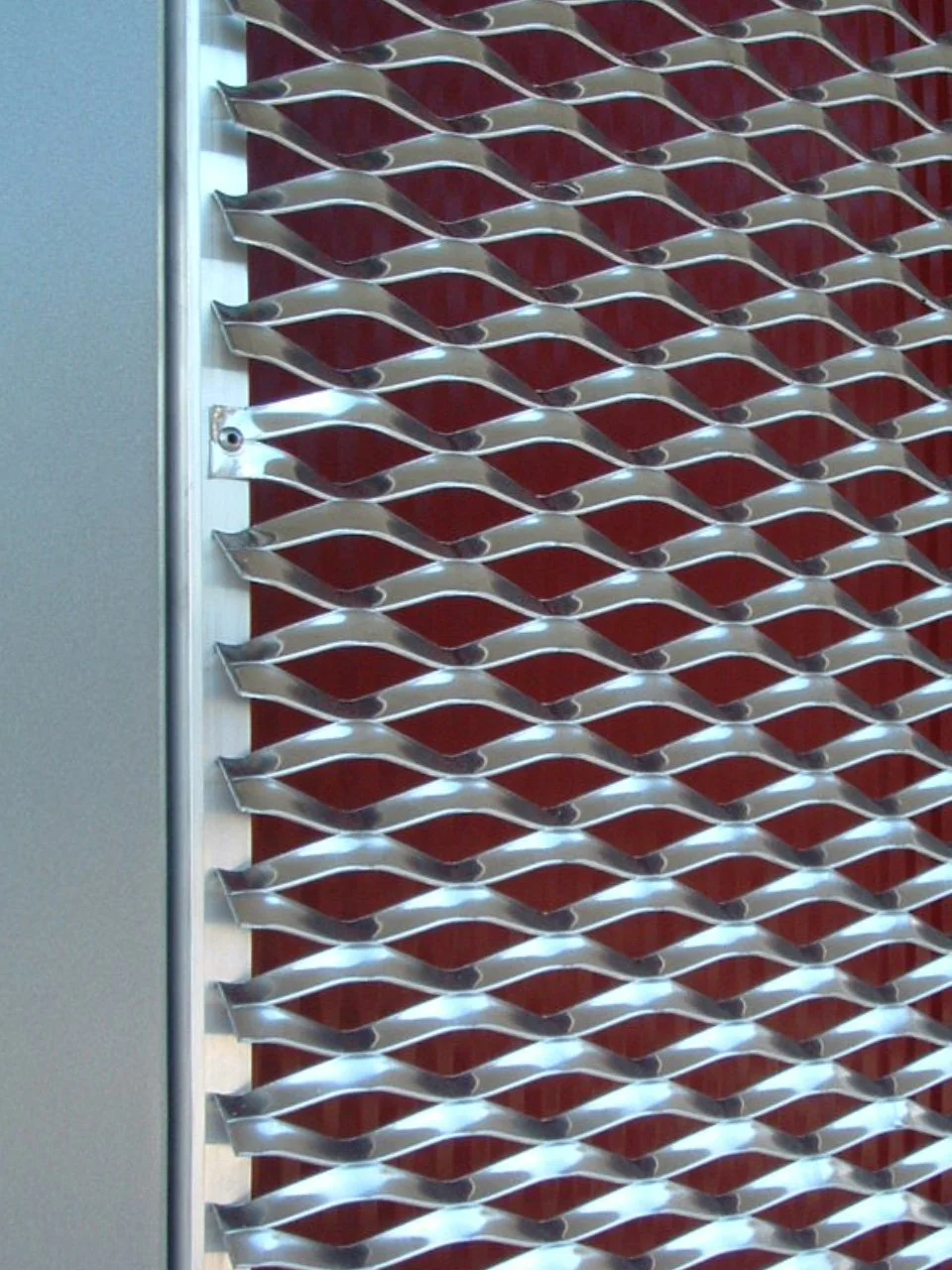 Metallgitter mit gewölbten Lamellen vor rotem Hintergrund.