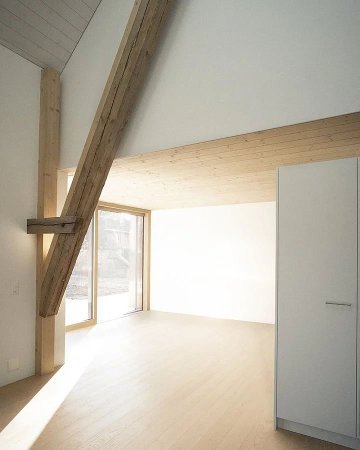 Ein heller, moderner Raum mit Holzdecke, Holzfußboden und großen Fenstern, die viel Tageslicht einlassen, sowie einem weißen Schrank.