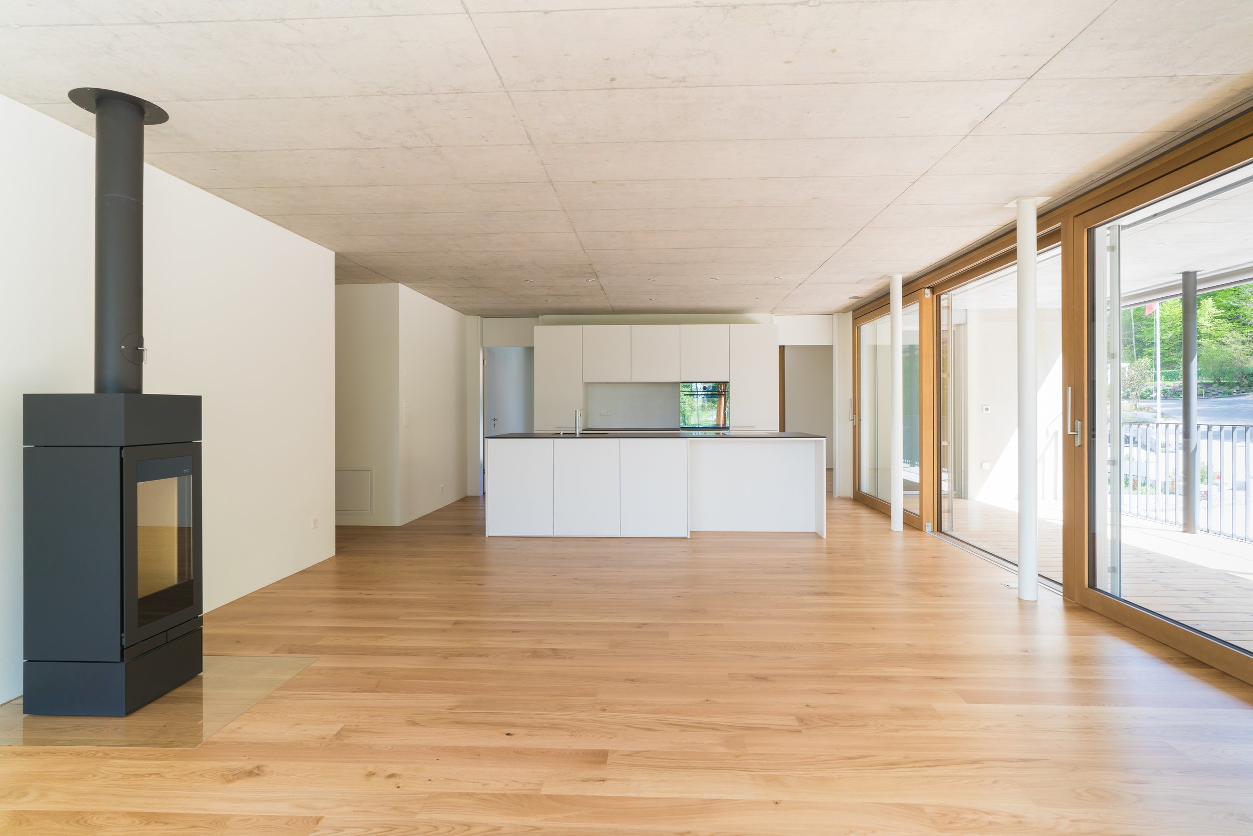 Moderne offene Küche mit weißen Schränken, Holzboden, großen Glasfenstern und einer Holz-Terrasse im Außenbereich.