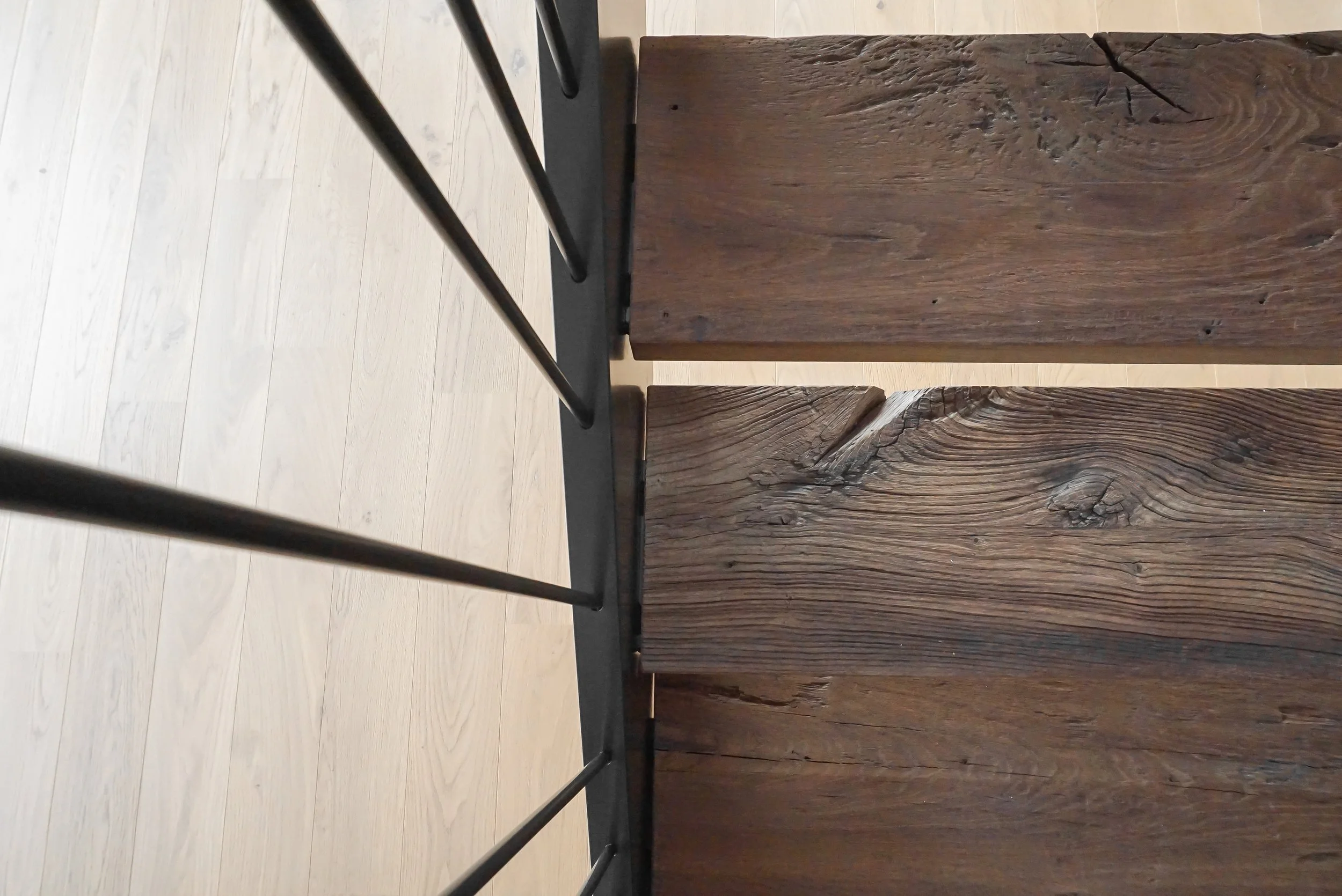 Blick auf die Seiten eines Tisches mit Holzmaserung, im Vordergrund eine schwarze Betonplatte, im Hintergrund ein heller Holzboden.