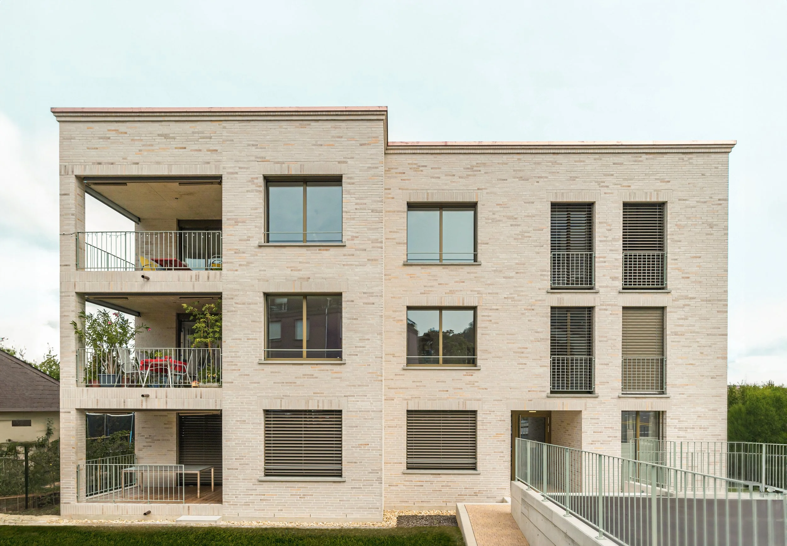 Mehrstöckiges modernes Wohngebäude mit Balkonen und großen Fenstern, aus Ziegelsteinen gebaut, mit Gartenfläche im Vordergrund