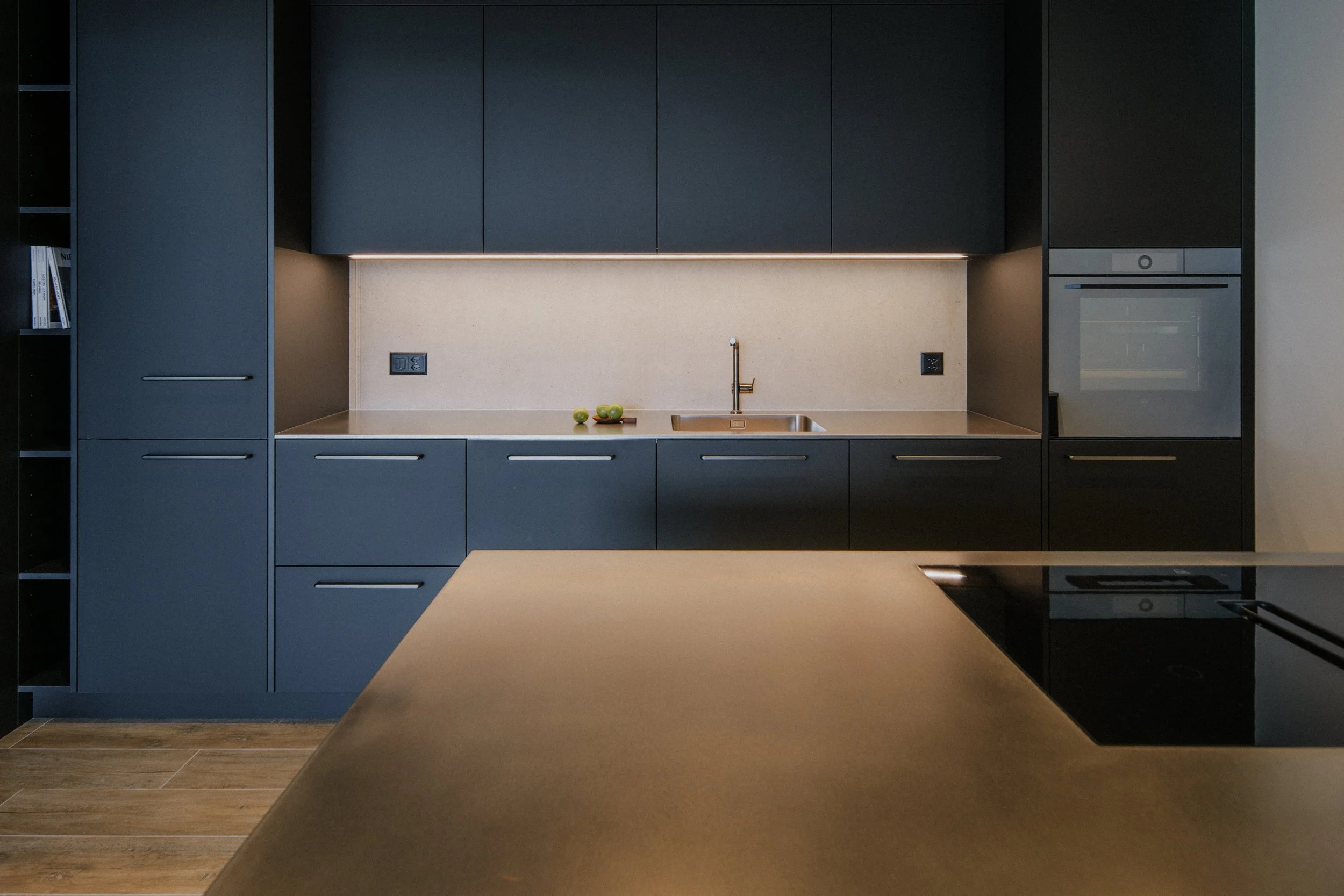 Moderne Küche mit schwarzen Schränken, beige Arbeitsplatte, Wasserhahn und drei grüne Äpfel auf dem Tresen.