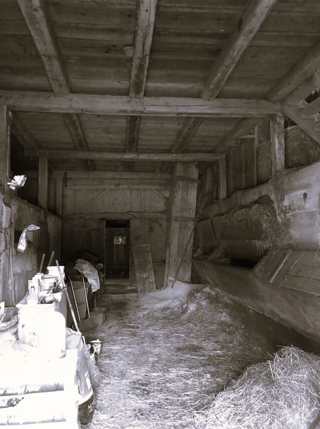 Innenaufnahme einer alten, verstaubten Scheune mit Holzdecke, Staub, Sägemehl und alten Werkzeugen an den Seitenwänden.