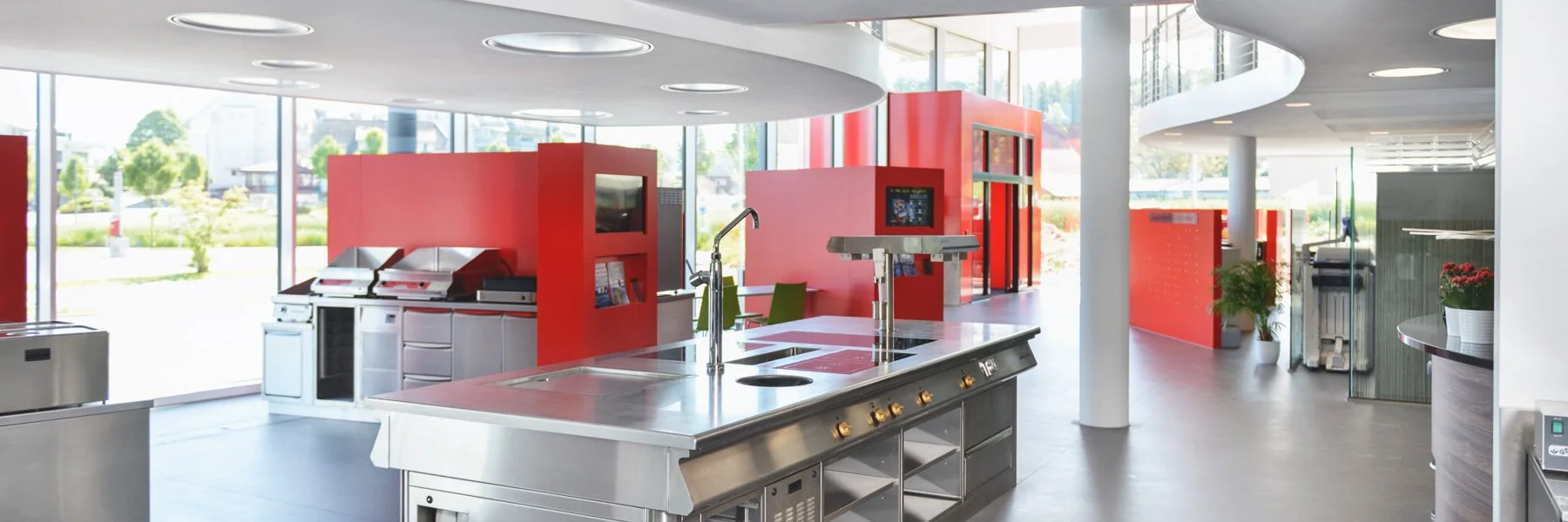 Moderne, helle Küche mit Edelstahlgeräten, rotem Akzentwand und großen Fenstern, die Tageslicht hereinlassen.