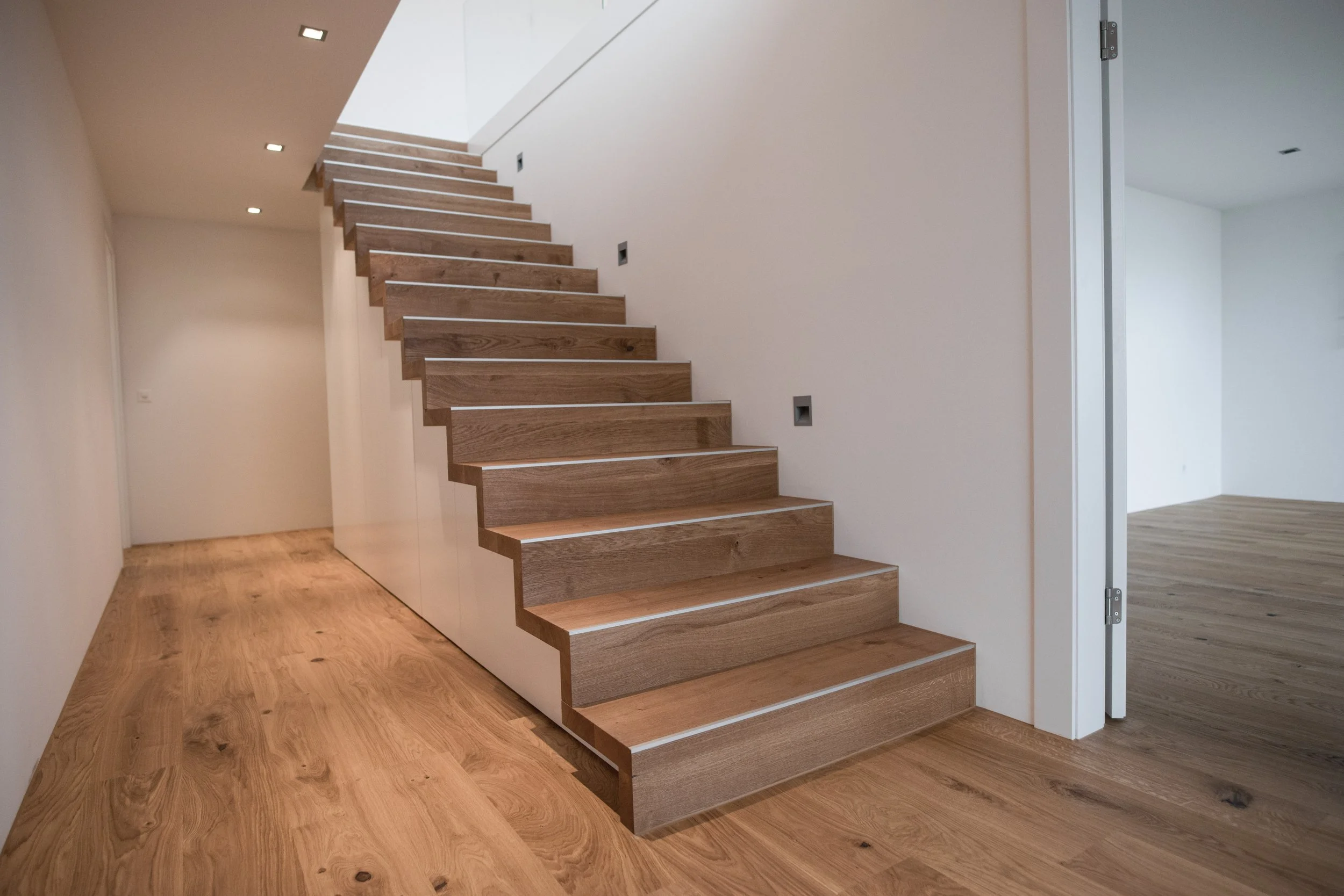 Innentreppen aus Holz in einem modernen, hellen Raum mit Holzboden und weißen Wänden.
