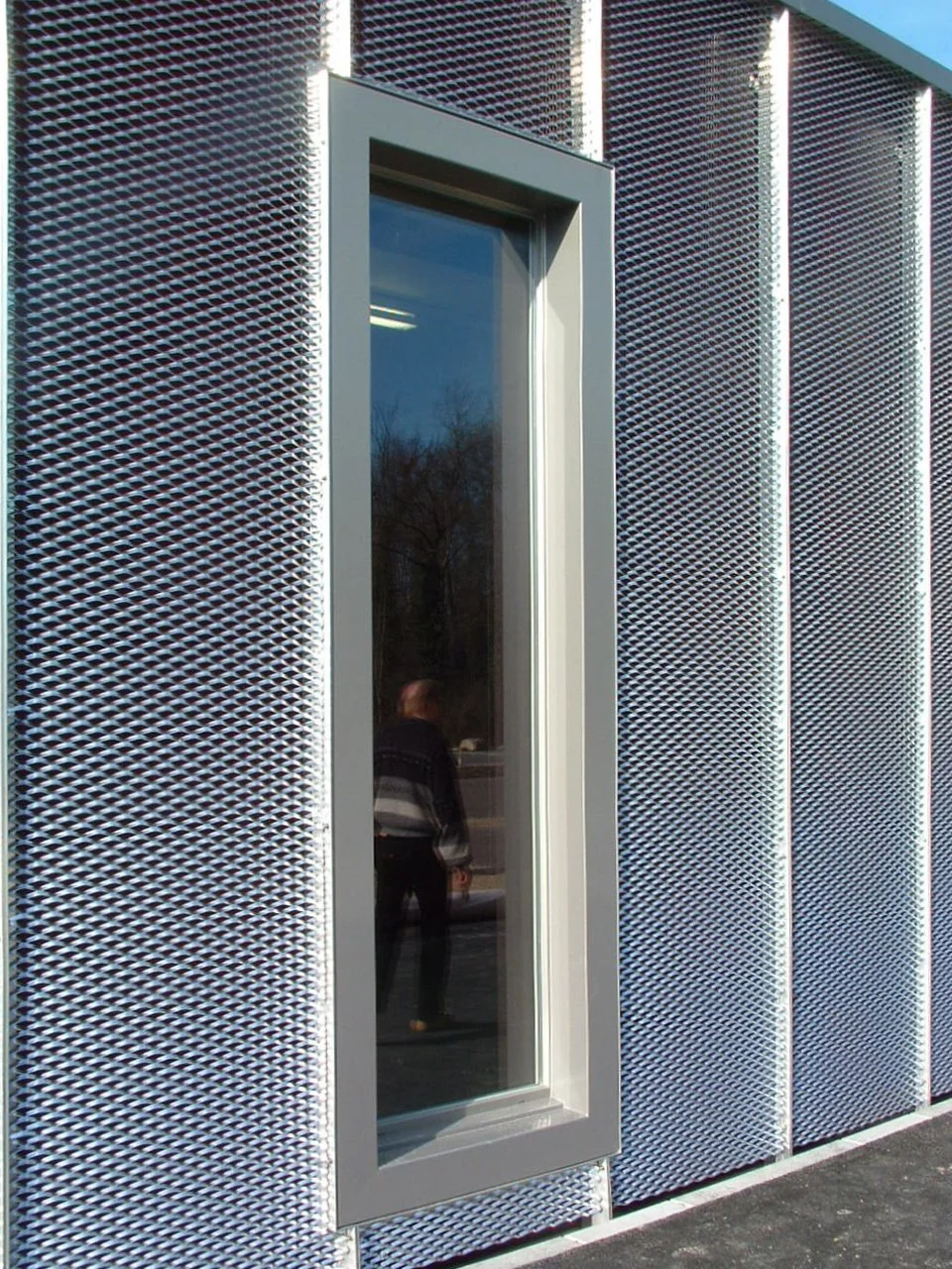 Außenansicht eines modernen Gebäudes mit perforierten Metallverkleidungen und einem schmalen Fenster.