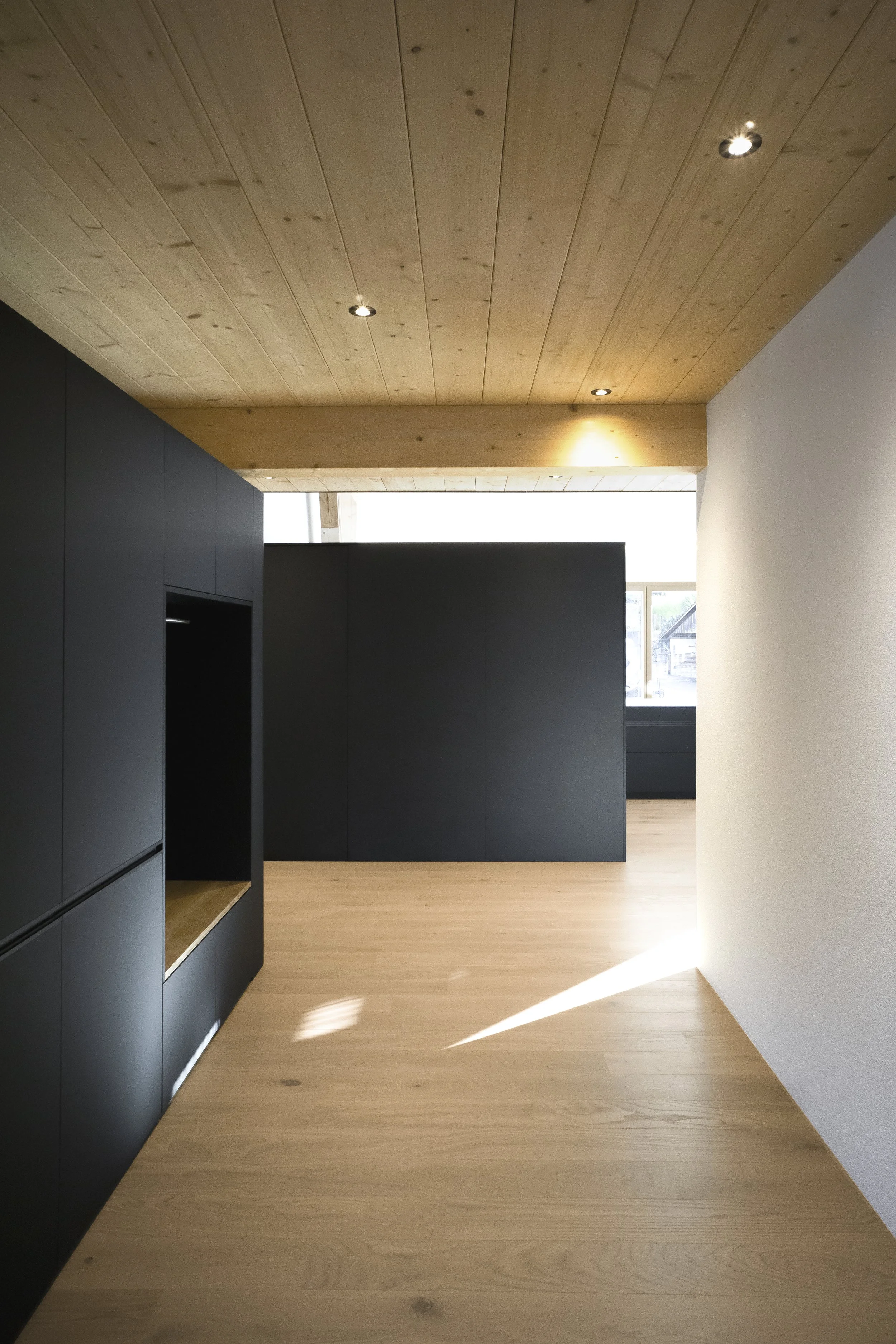 Innenraum mit Holzdecke, schwarzen Schränken und hellem Holzboden, Tageslicht strömt durch Fenster