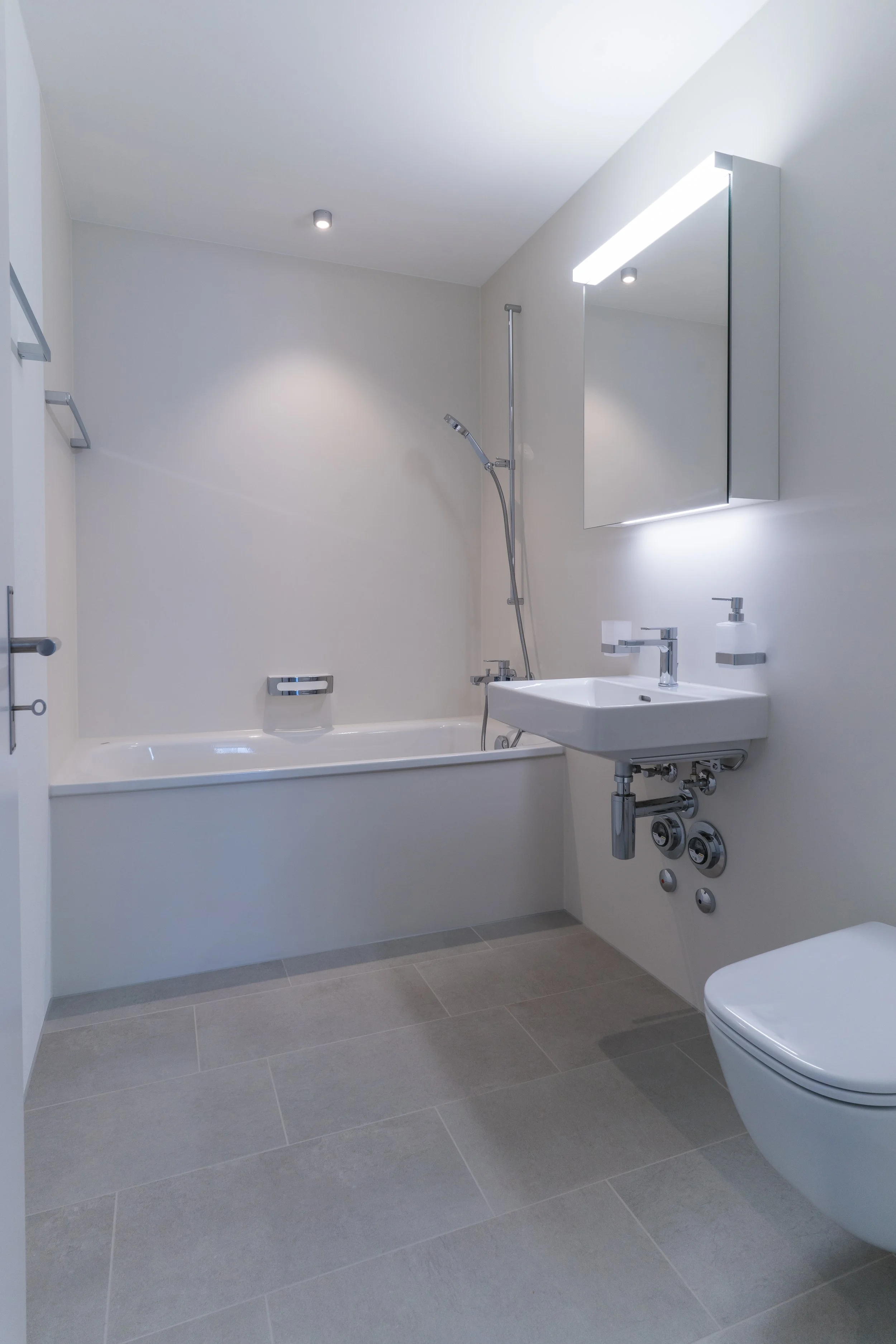 Modernes Badezimmer mit Badewanne, Waschbecken, Spiegel, Handtuchhalter und Toilette, in neutralen Farben gestaltet.
