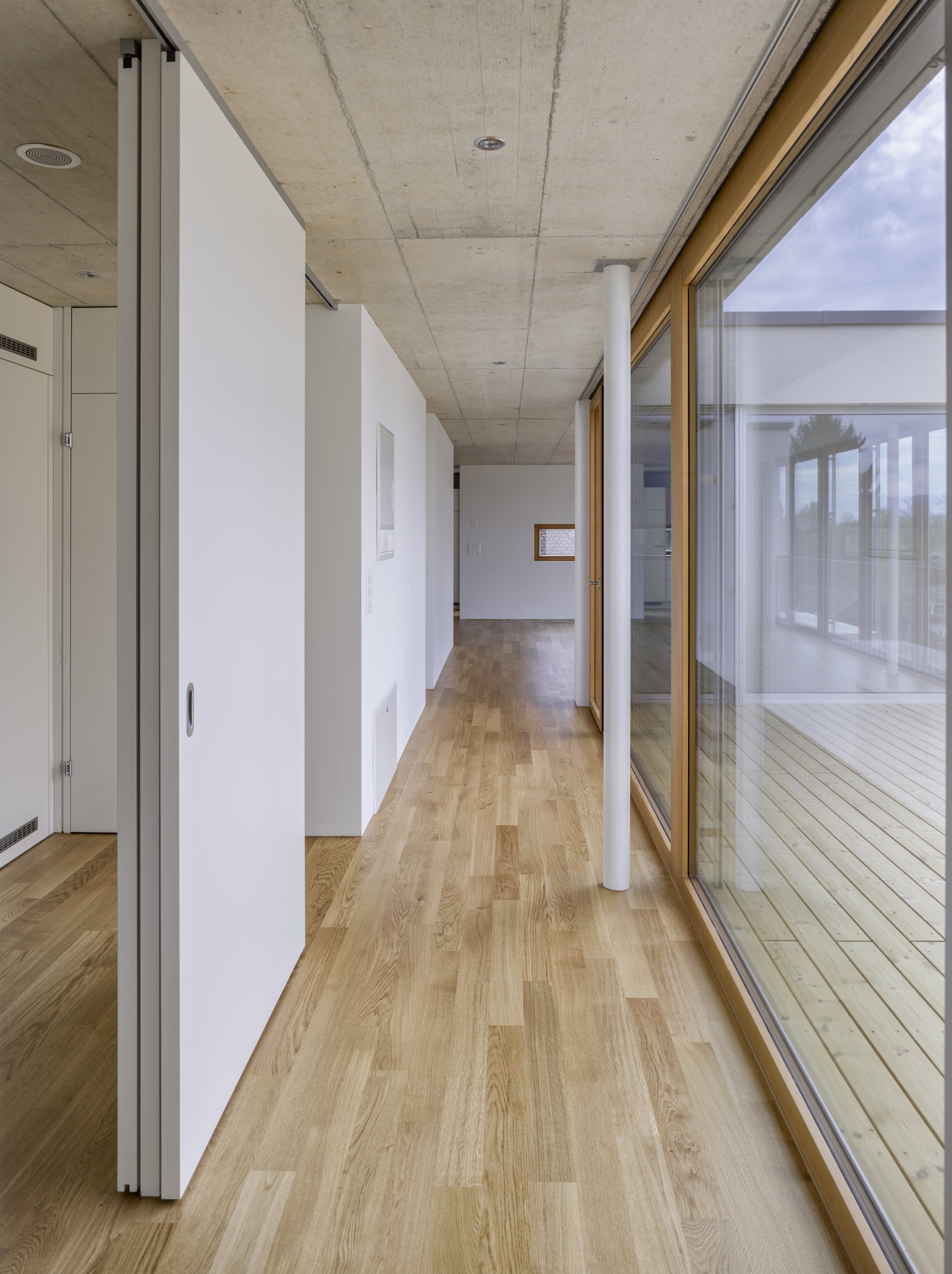 Moderner Innenraum mit Holzboden, großen Fenstern und weißen Wänden.