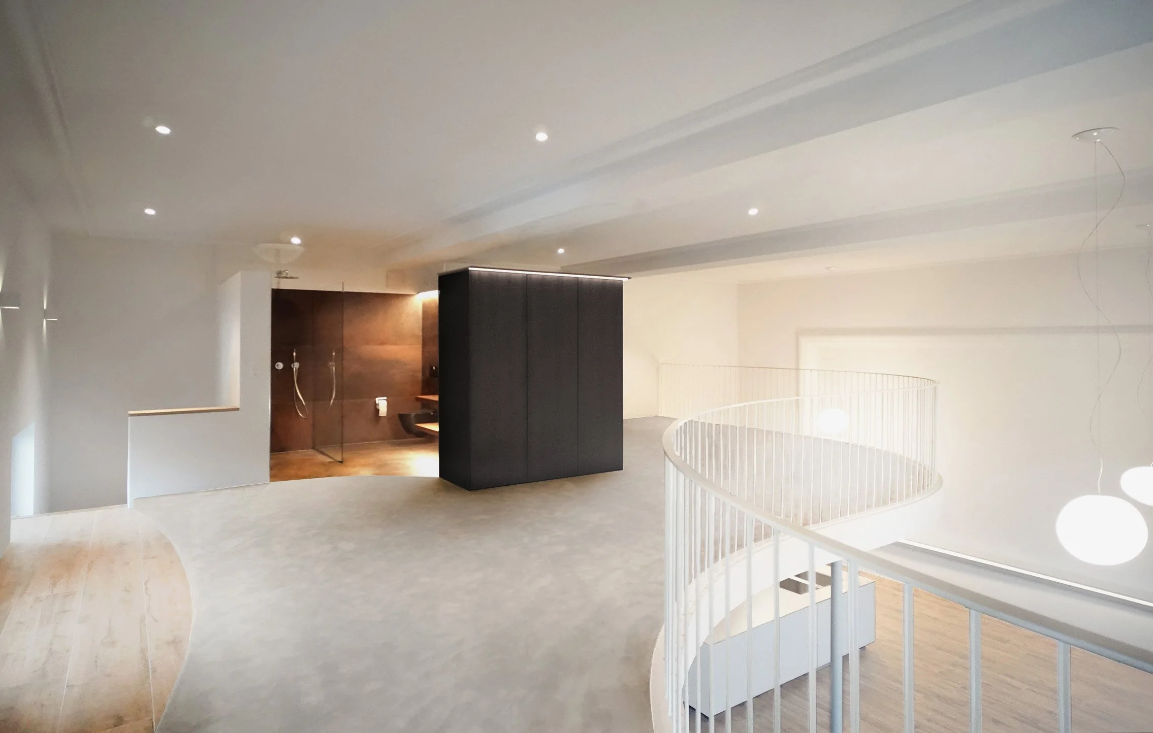 Innenraum eines modernen Hauses mit weißer Treppe und dunklem Wandschrank, helle Wände und Decken mit eingebauten Leuchten.