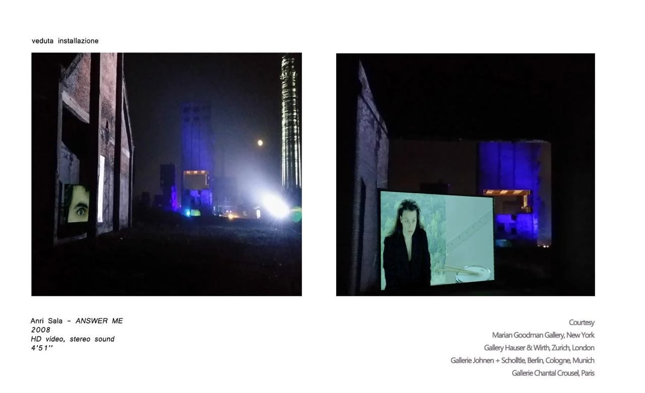 Dark gallery space with video screens showing close-up of eyes and a woman, illuminated by blue and white lights, with an outdoor scene in the background.