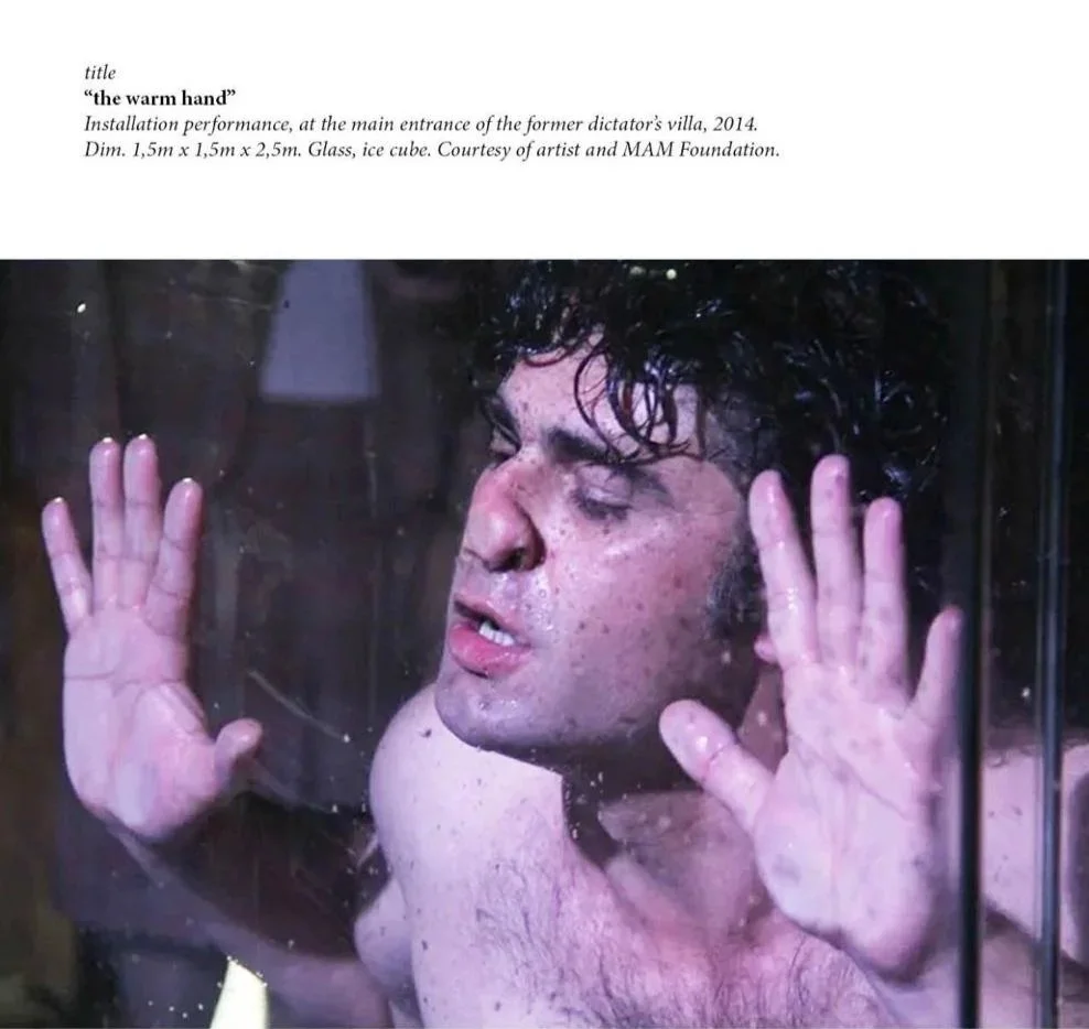 A man with curly dark hair and freckles presses his face and hands against a glass ice cube, with a look of concentration or emotion.