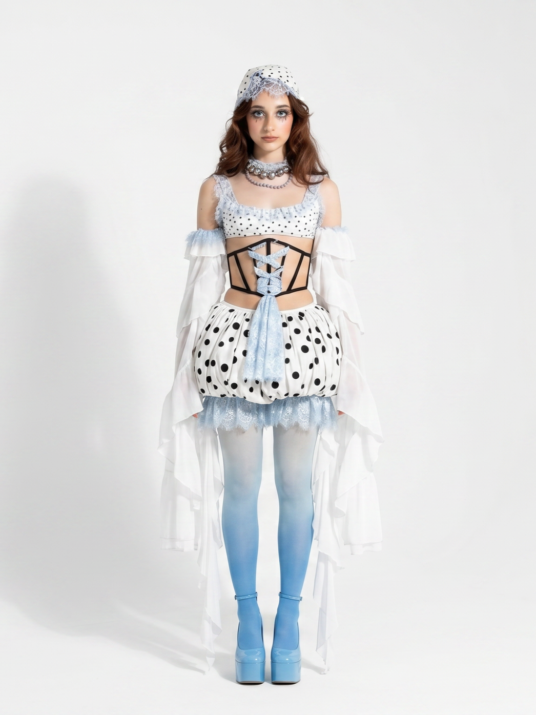 A young woman in a whimsical, polka dot themed costume with layers of white and black, blue tights, blue platform heels, and matching accessories including a hat and lace-trimmed petticoat, standing against a plain white background.