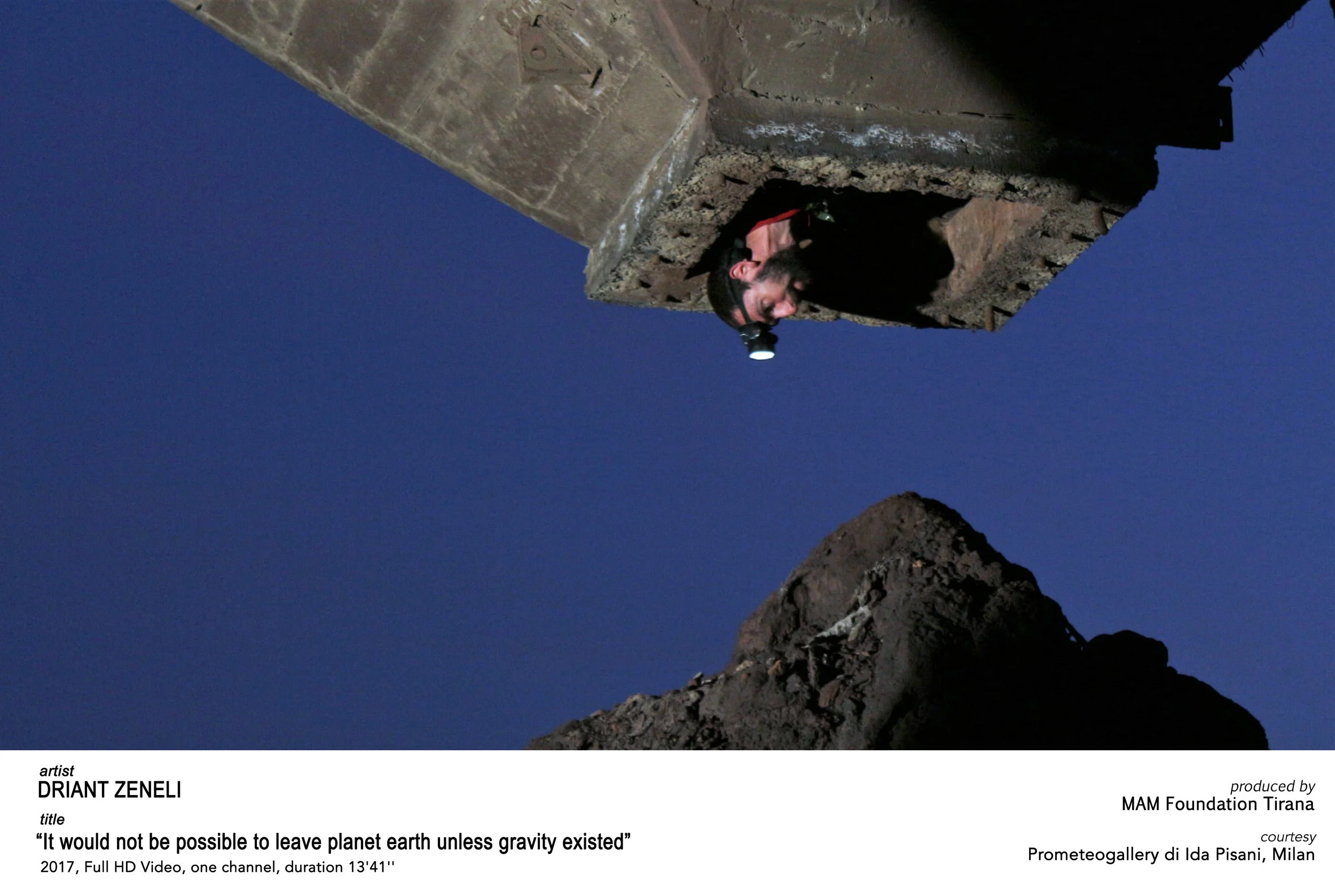 A person with a headlamp looking out from a hole in a rocky structure against a dark blue sky.