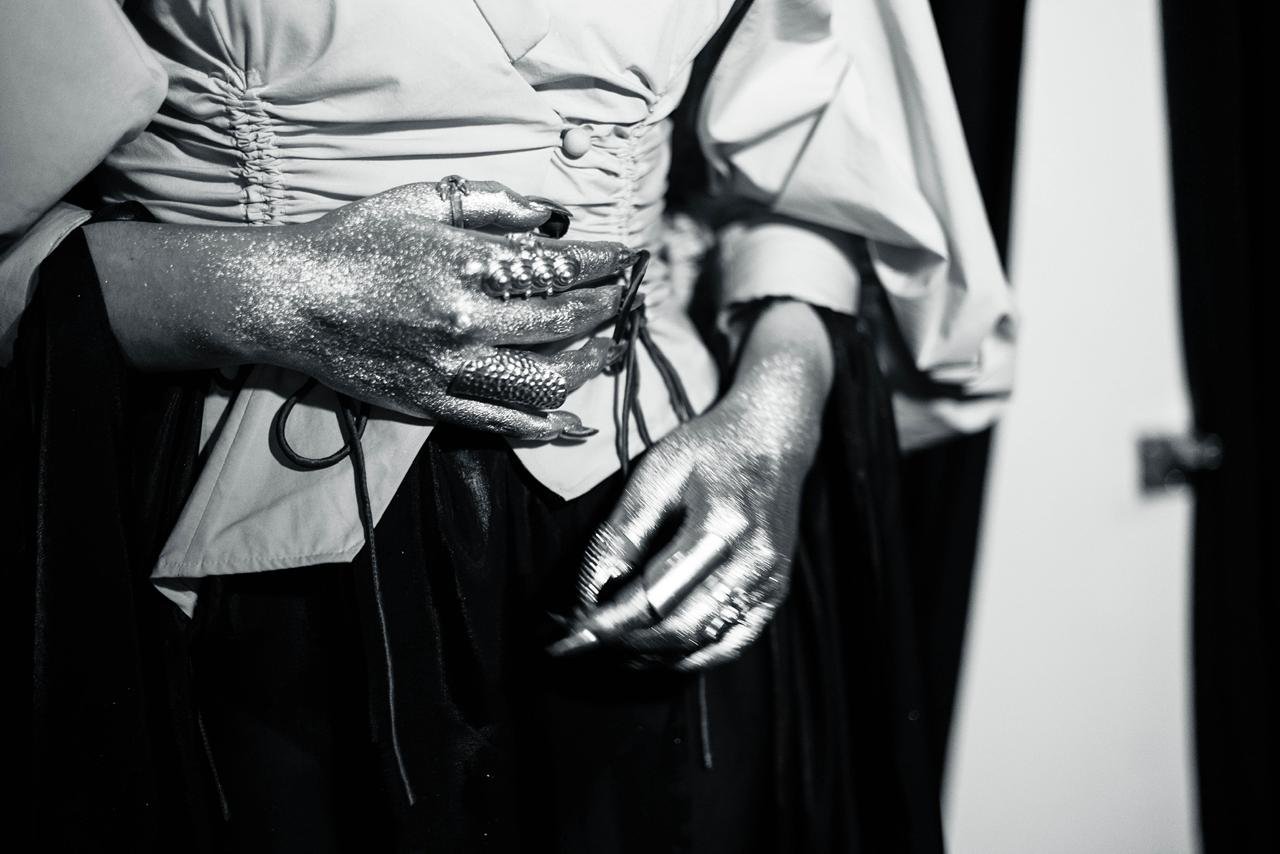 Person with glittery silver hands, wearing rings, holding a telephone.
