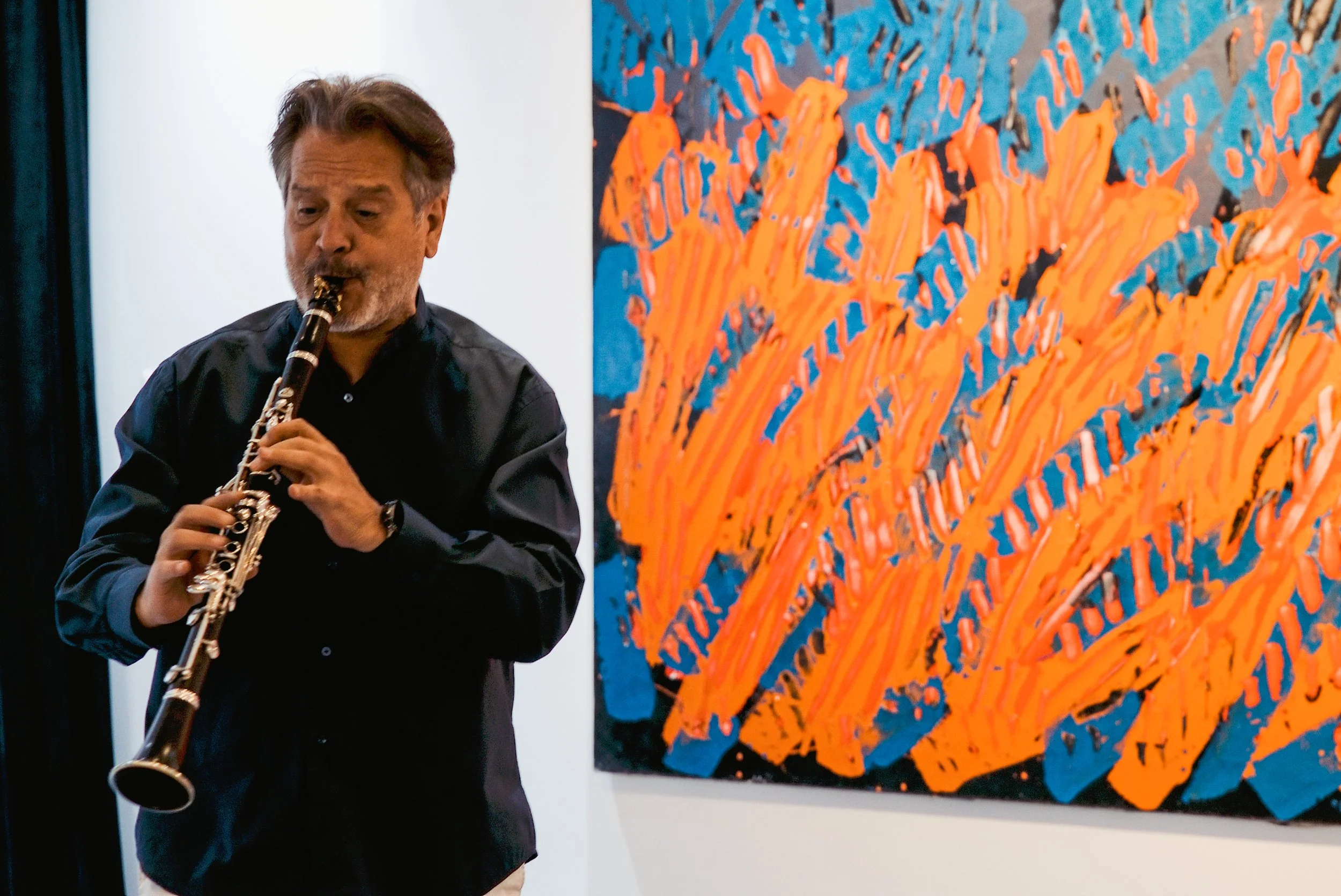 A man playing a clarinet standing in front of colorful abstract artwork.