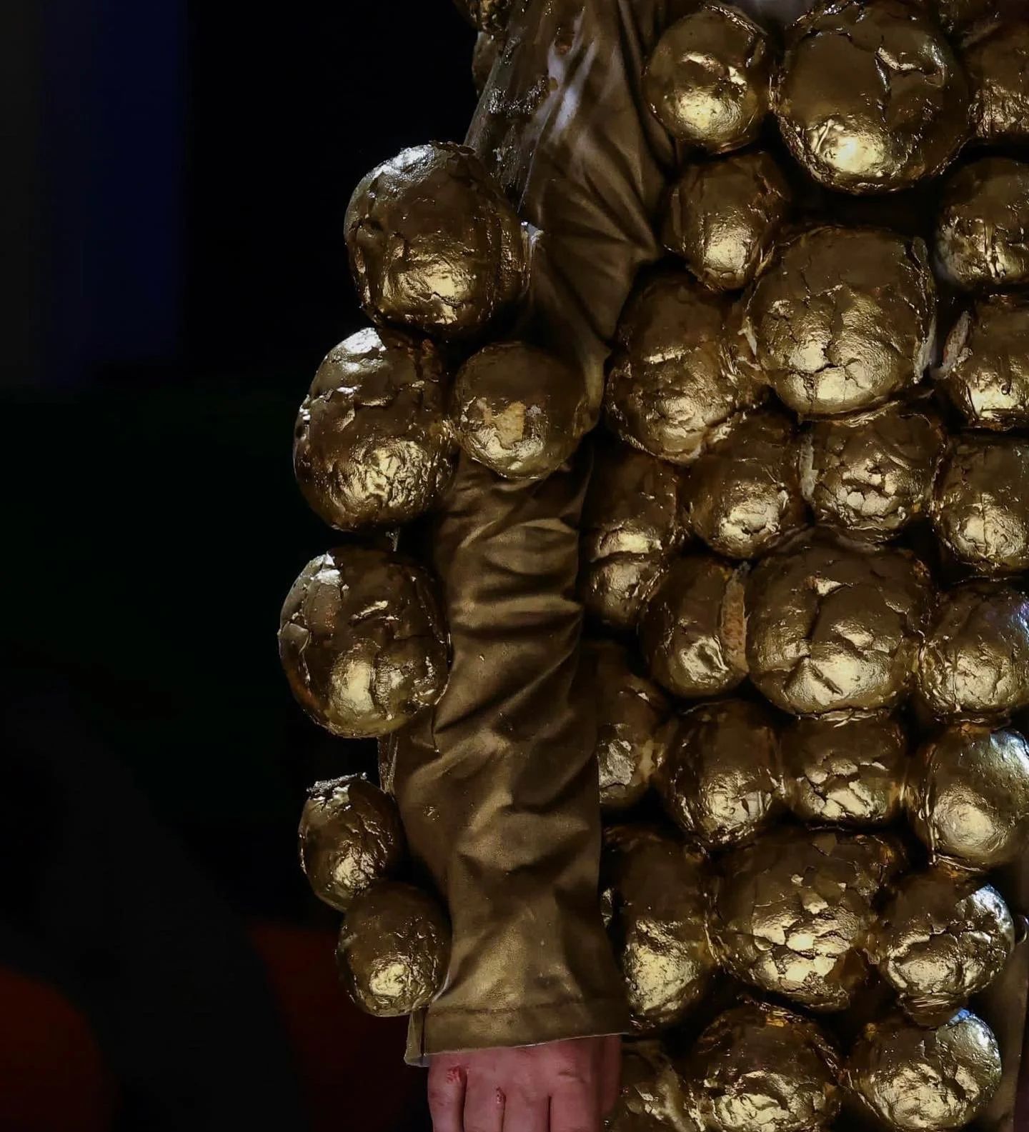 Close-up of a person holding a gold-colored bouquet made of metallic, spherical objects, wrapped in a dark cloth.